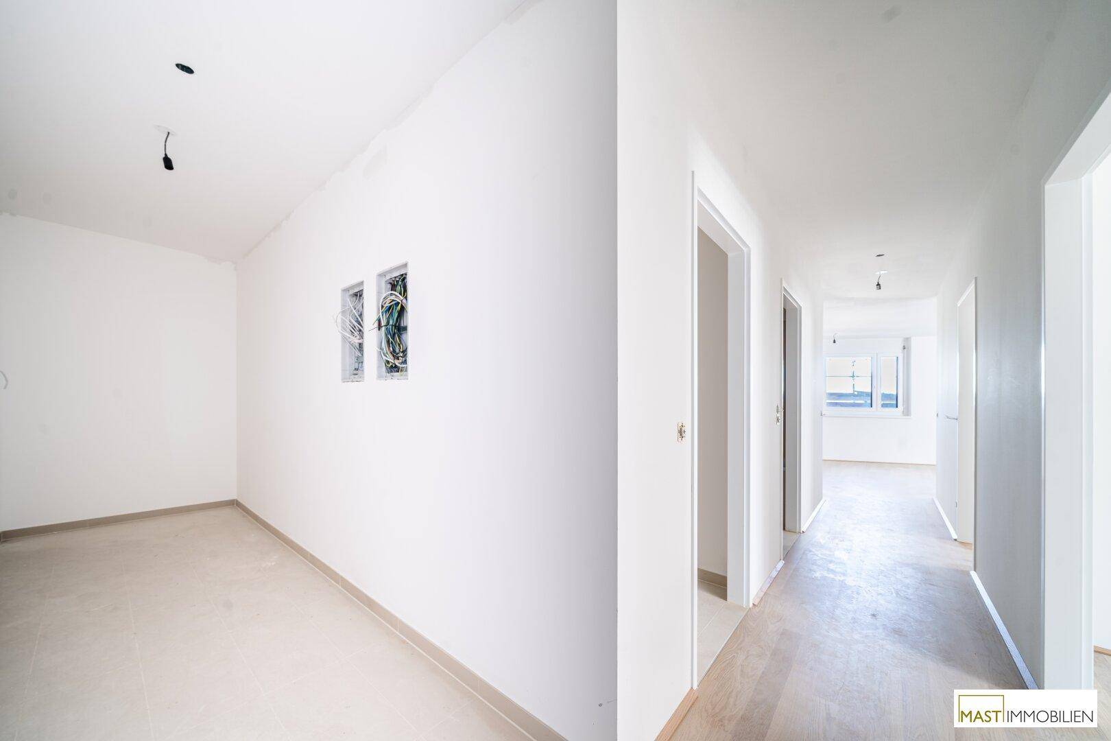 Heller Flur mit weißen Wänden und hellem Boden, der zu weiteren Zimmern in der Wohnung führt.