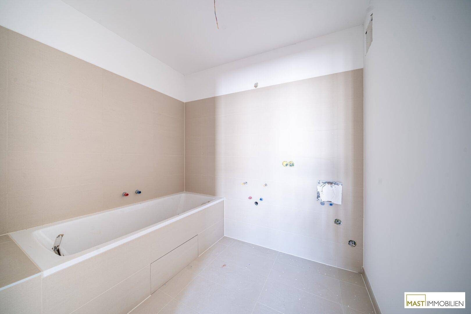 Badezimmer im Bau mit eingebauter Badewanne und beigefarbenen Fliesen an den Wänden.