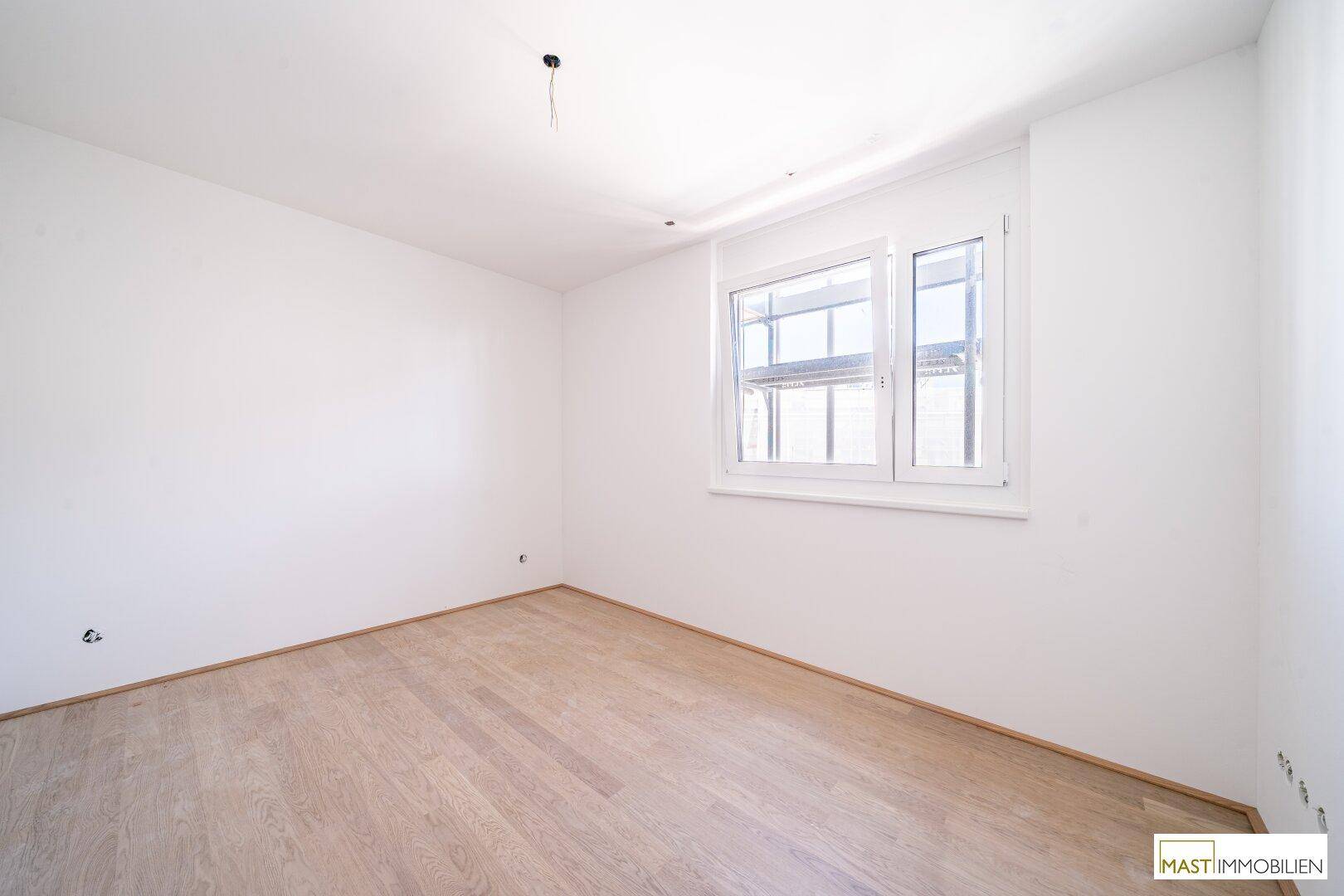 Helles, unmöbliertes Schlafzimmer mit Parkettboden und großem Fenster für viel Tageslicht.