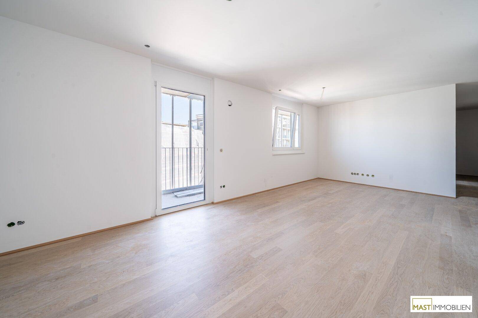 Heller, unmöblierter Wohnraum mit hellem Parkettboden und Zugang zu einem französischen Balkon.