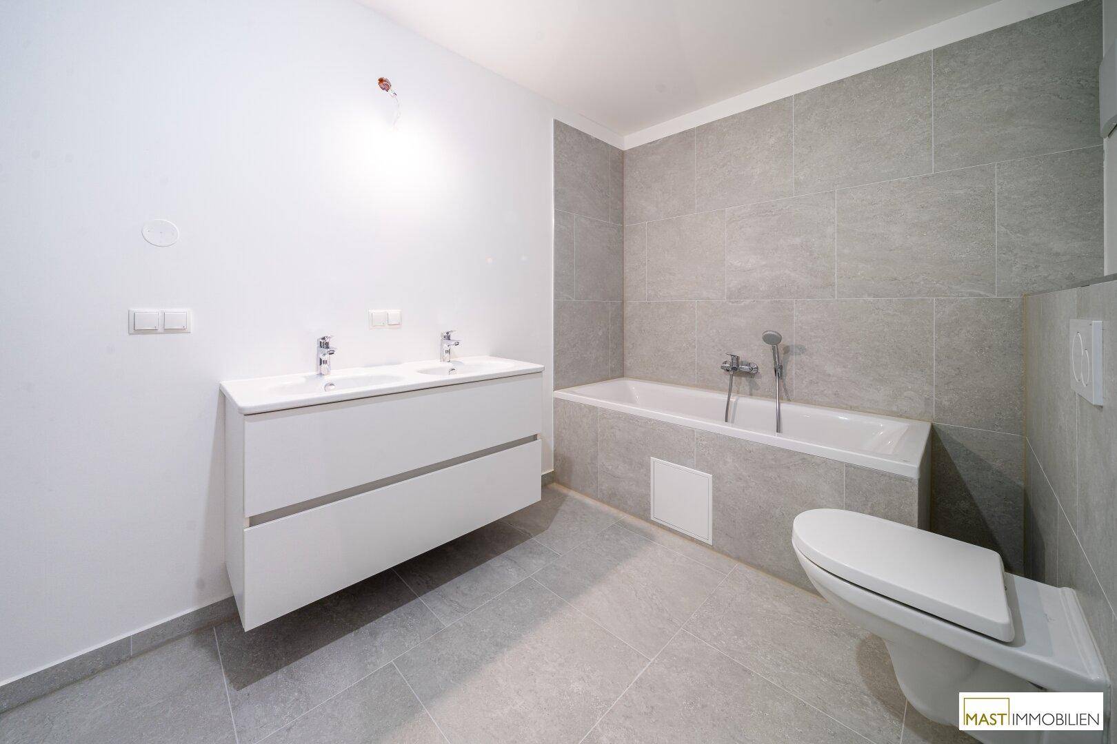 Geräumiges Badezimmer mit Badewanne, Doppelwaschbecken und modernen Fliesen.