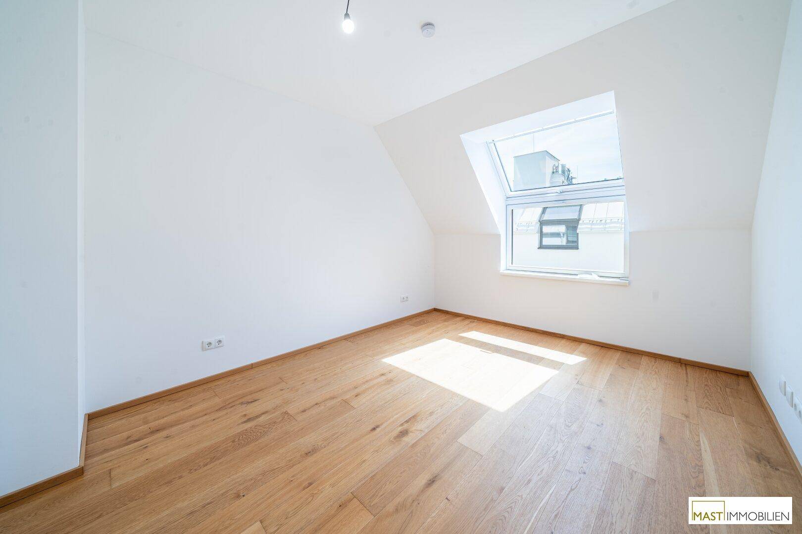Helles Schlafzimmer im Dachgeschoss mit Holzboden und großem Dachfenster.