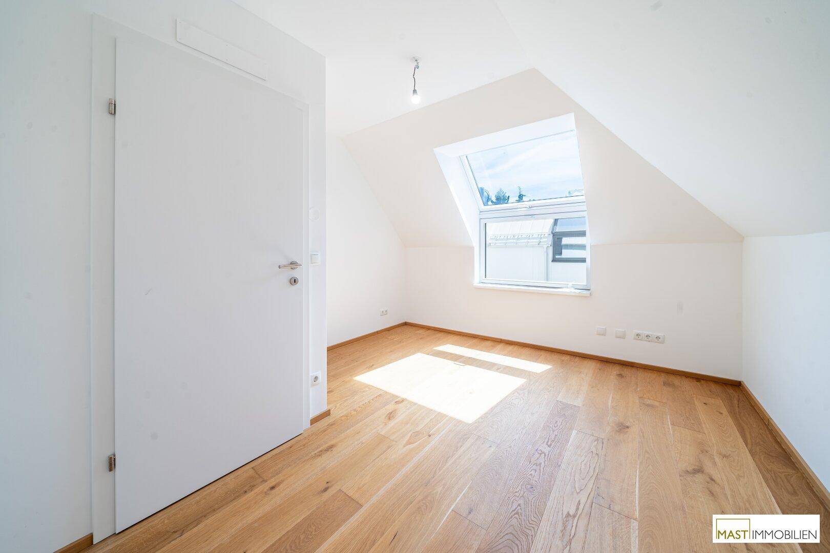 Lichtdurchflutetes Schlafzimmer mit Holzboden und schräger Decke im Dachgeschoss.