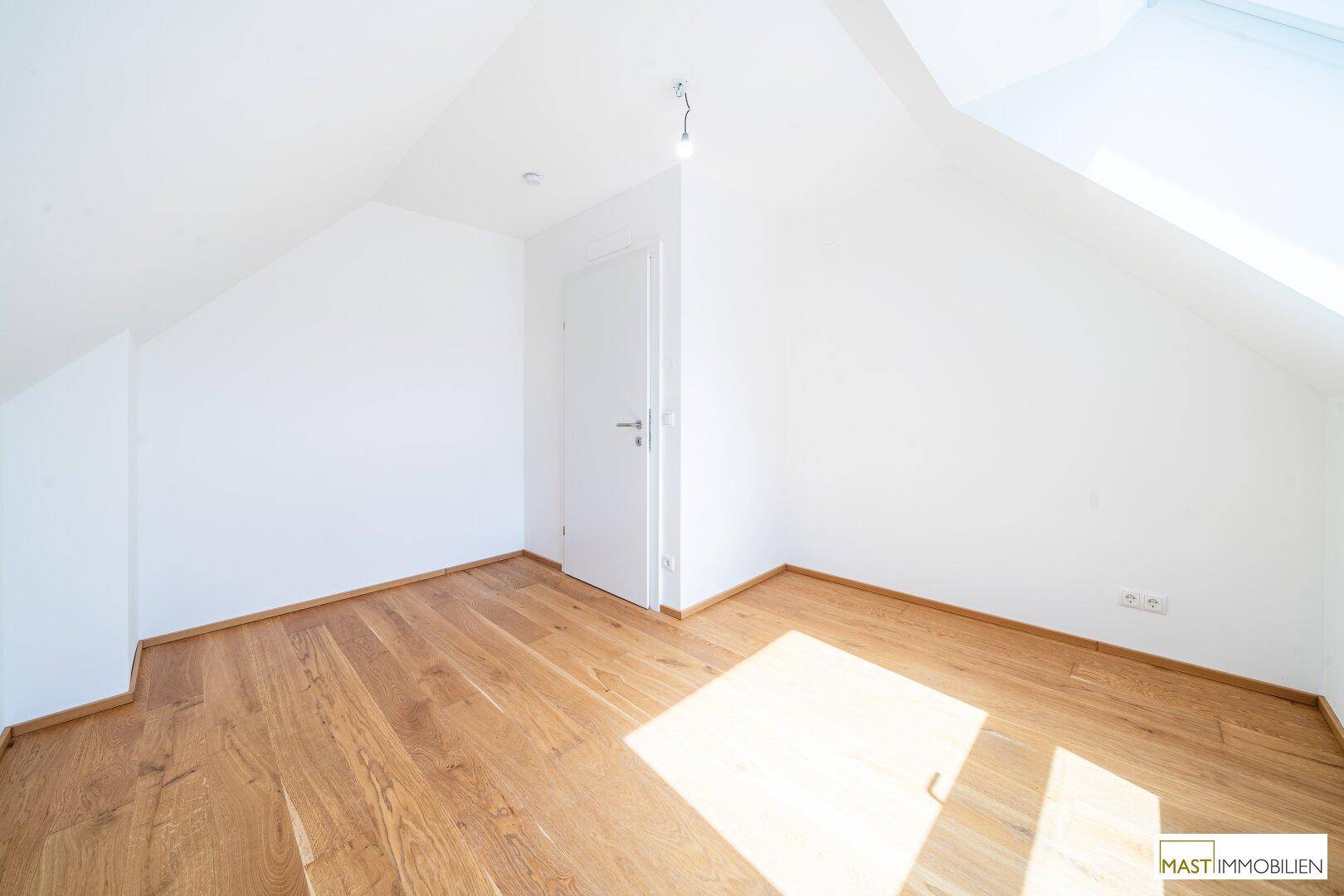 Gemütliches Schlafzimmer mit Holzboden und viel Tageslicht durch das Dachfenster.