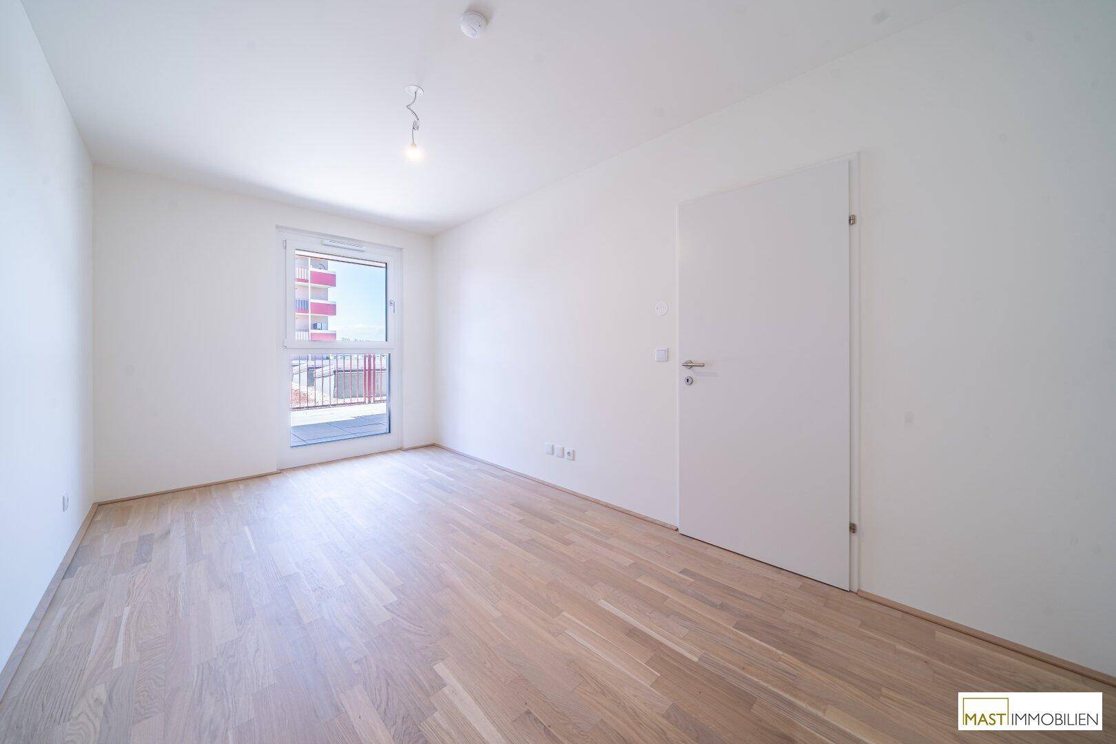 Helles Schlafzimmer mit Holzboden, weißen Wänden und direktem Zugang zum Balkon.