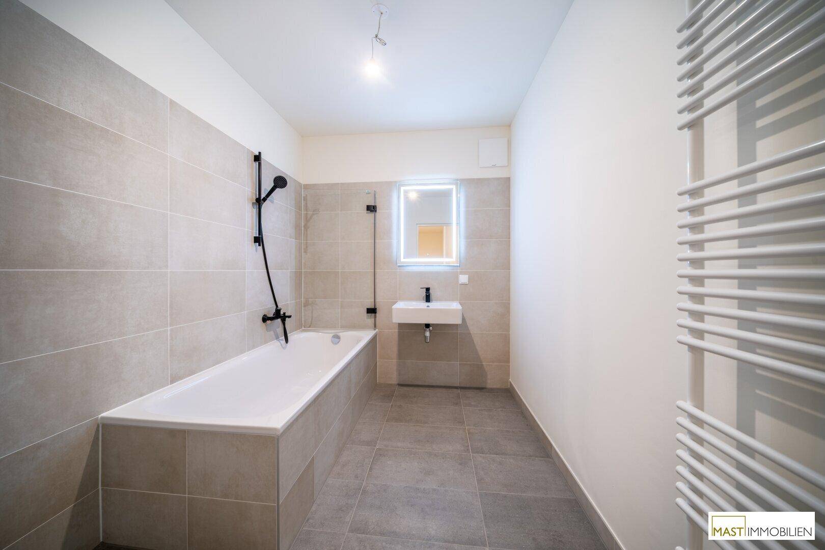 Modernes Badezimmer mit Badewanne, beleuchtetem Spiegel und beheiztem Handtuchhalter.