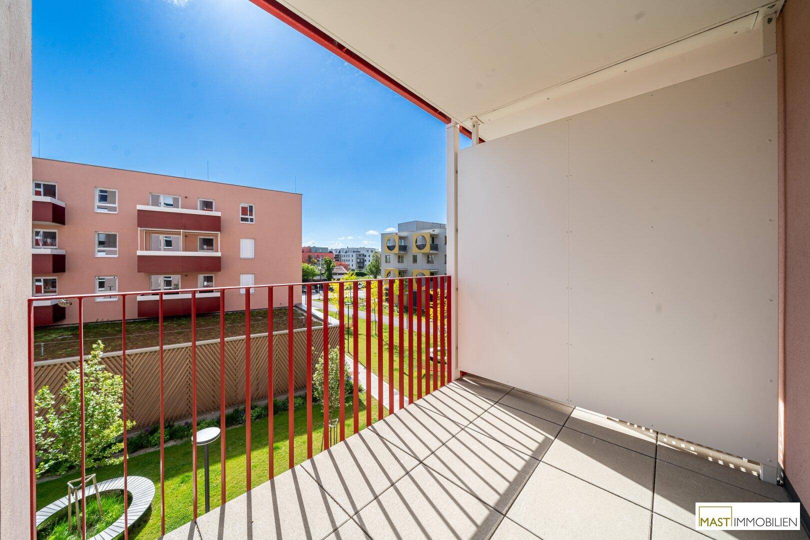 Sonniger Balkon mit rotem Geländer und Blick auf die umliegenden Gebäude.