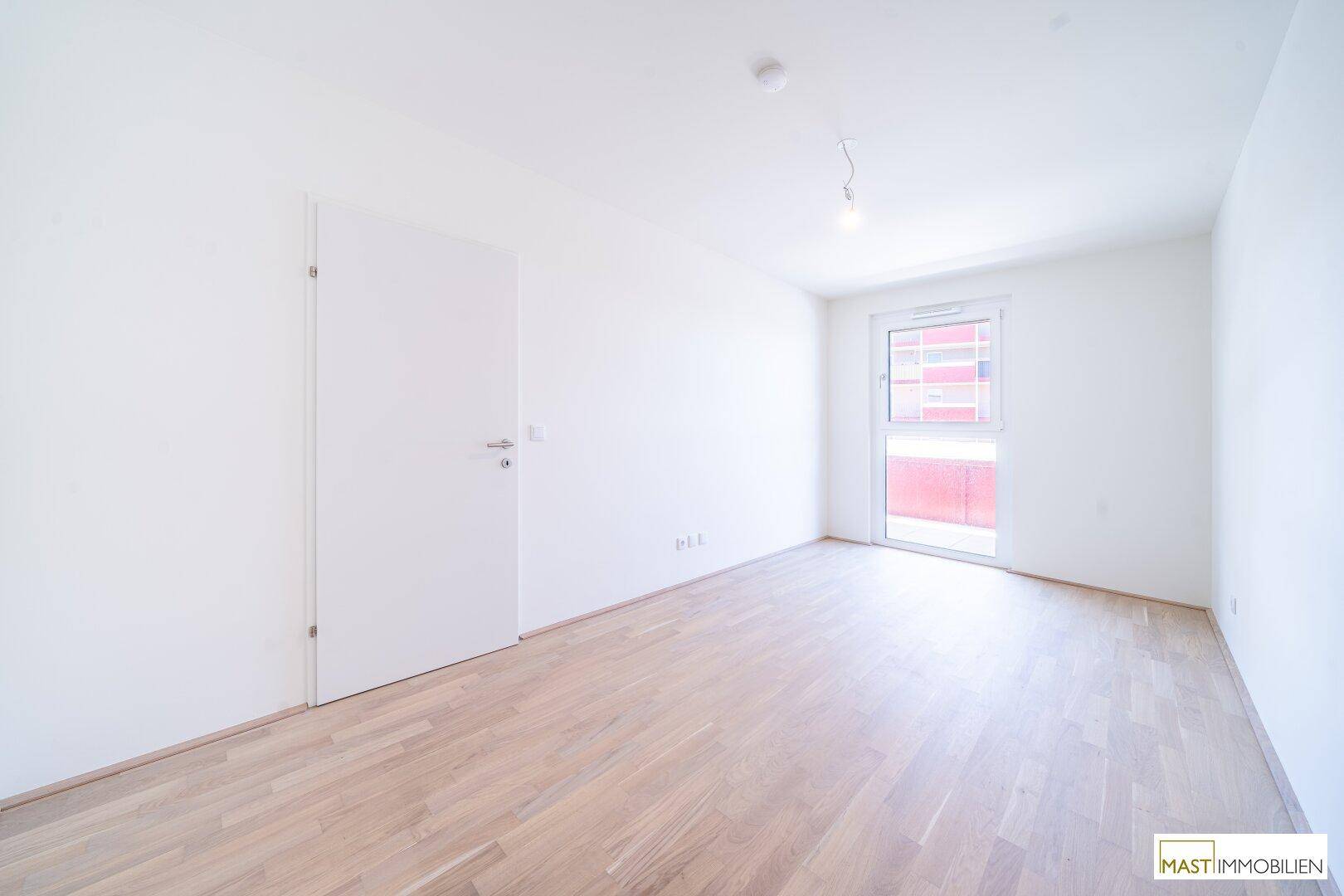 Leeres Schlafzimmer mit hellem Parkettboden und großem Fenster, ideal für individuelle Einrichtung.
