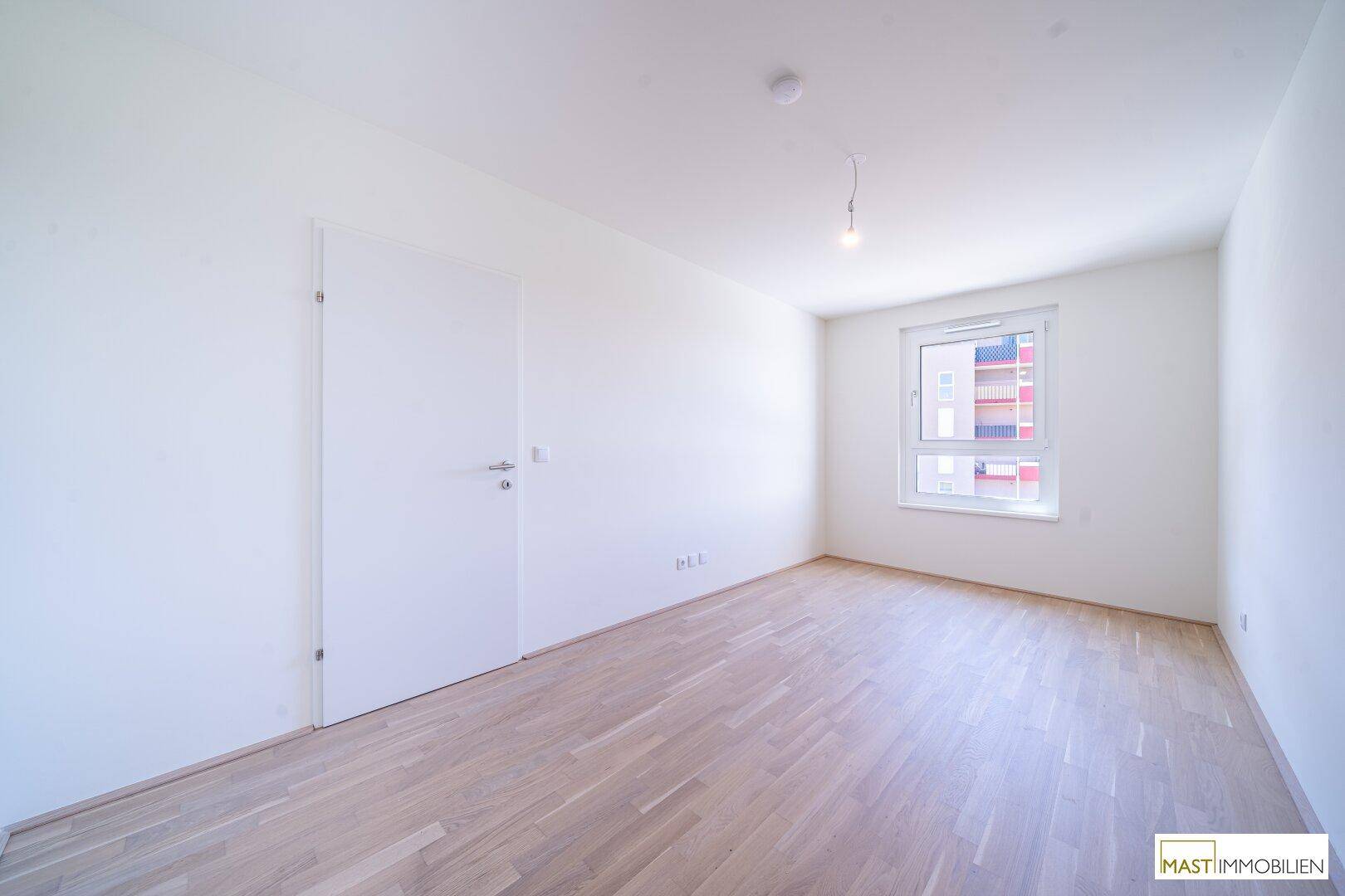 Helles Schlafzimmer mit Parkettboden und großem Fenster, bereit zur individuellen Gestaltung.