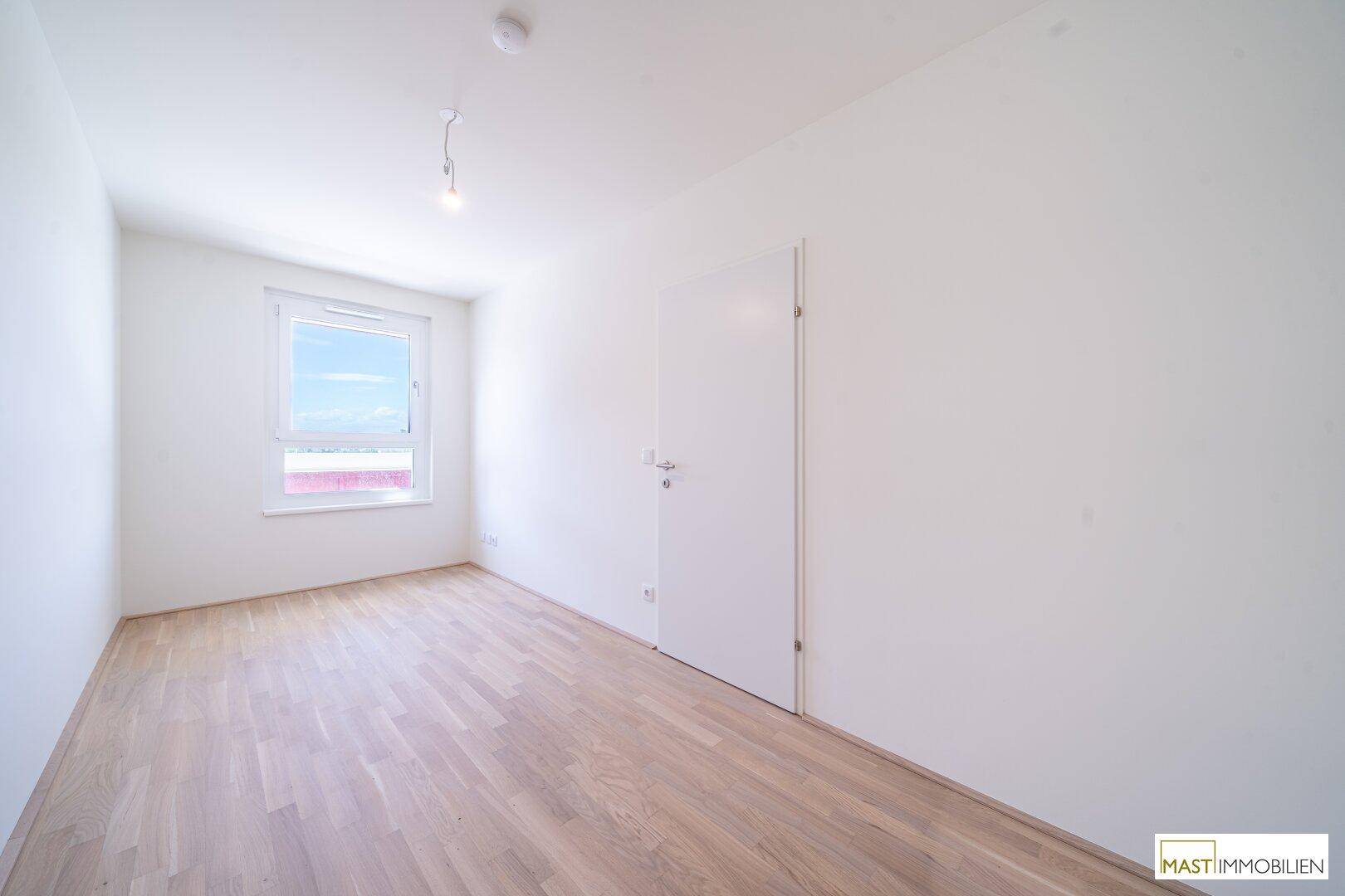 Ein weiteres helles Schlafzimmer mit Parkettboden und Fenster, ideal für Gäste oder Kinder.
