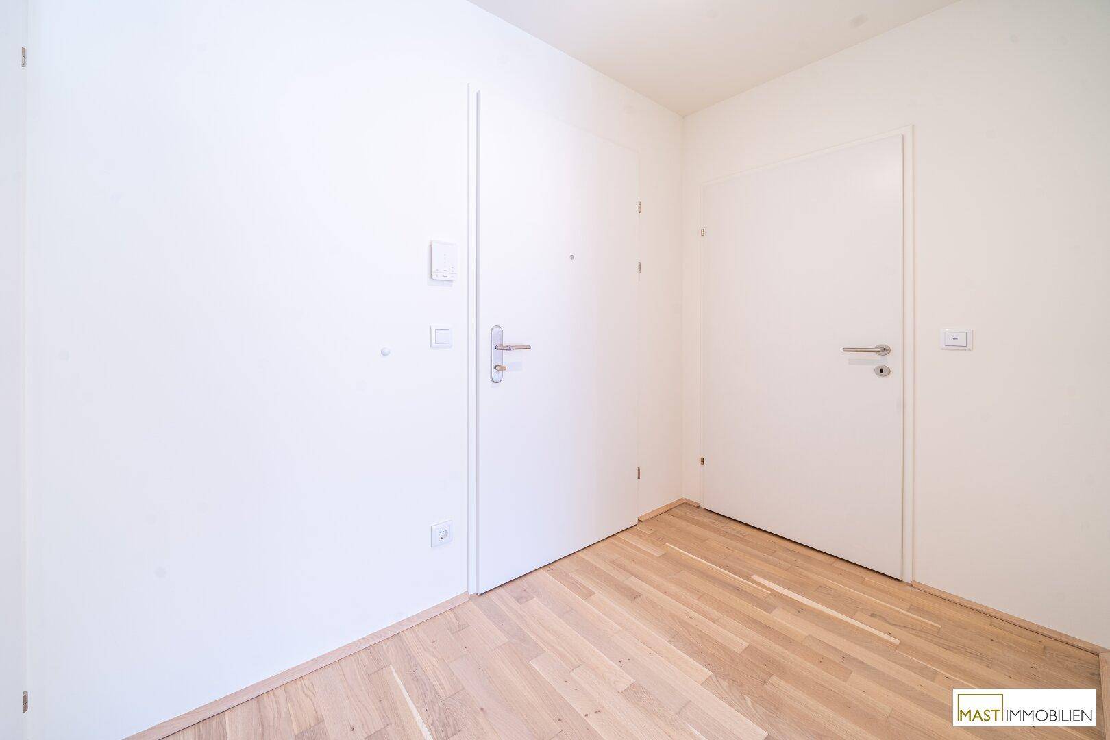 Heller Flur mit zwei weißen Türen und modernem Holzparkettboden.