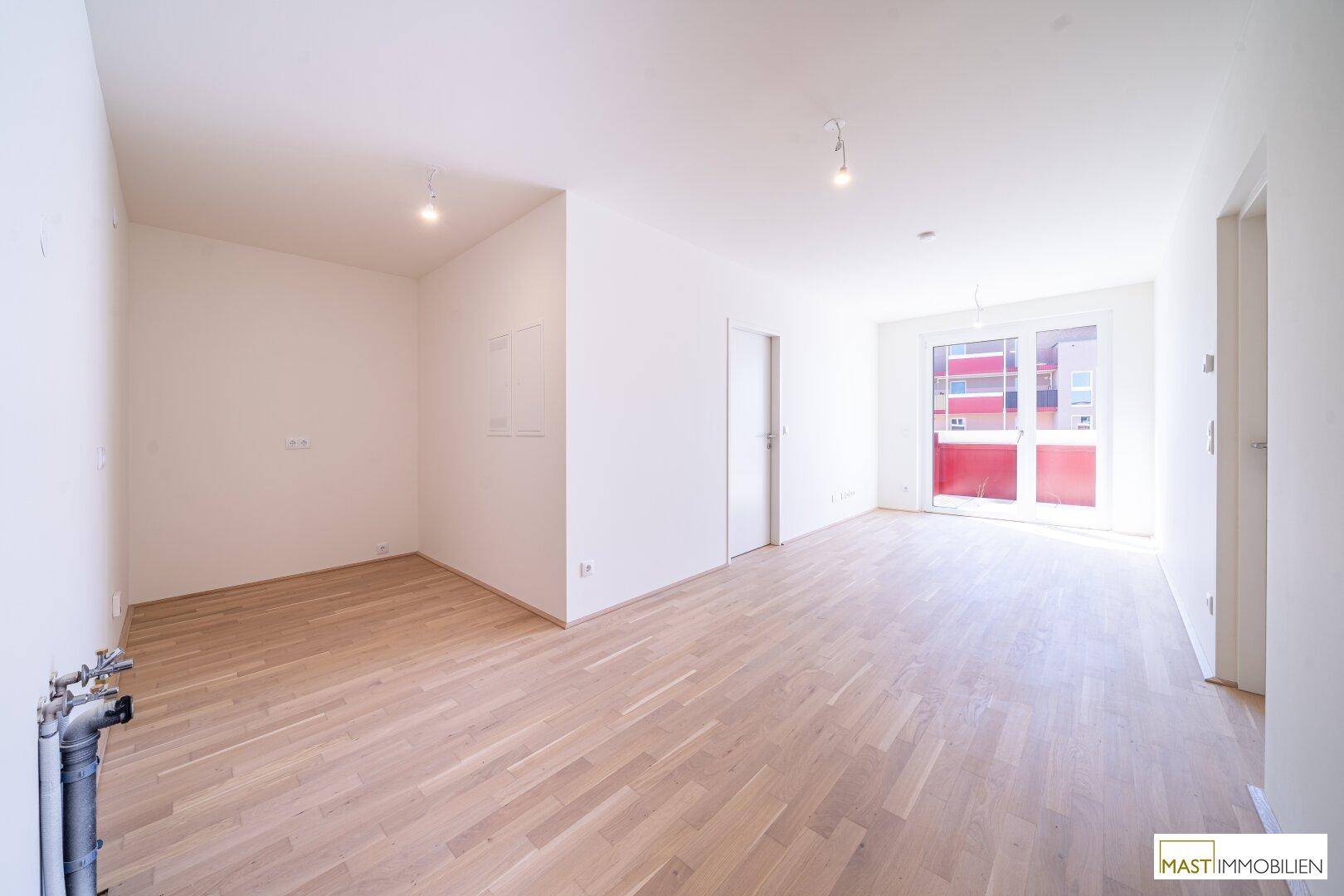 Heller, leerer Wohnbereich mit Parkettboden und Zugang zu einem Balkon oder einer Terrasse.