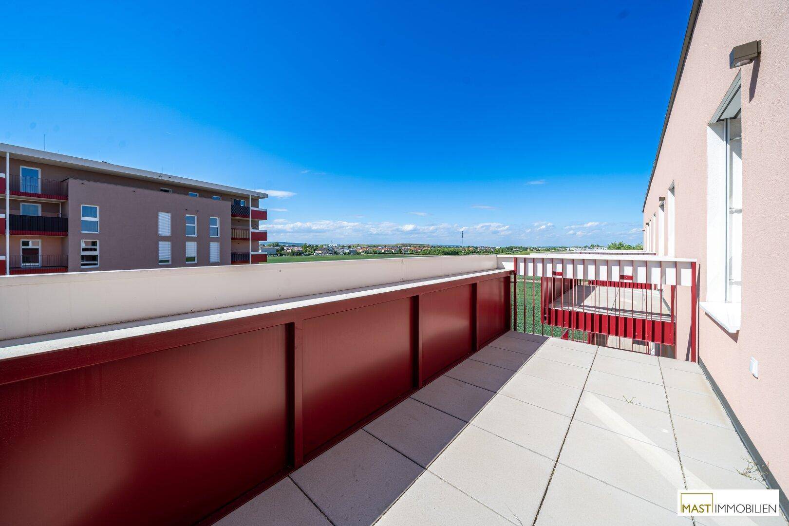 Großer Balkon mit Fliesenboden und weitem Blick über die umliegende Landschaft und Gebäude.