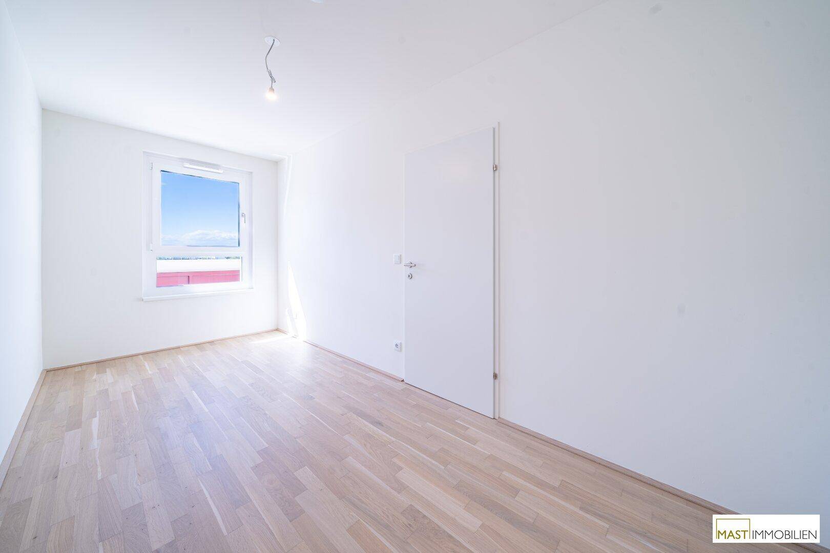 Weiteres helles Zimmer mit Parkettboden und großem Fenster, ideal als Schlaf- oder Arbeitszimmer.