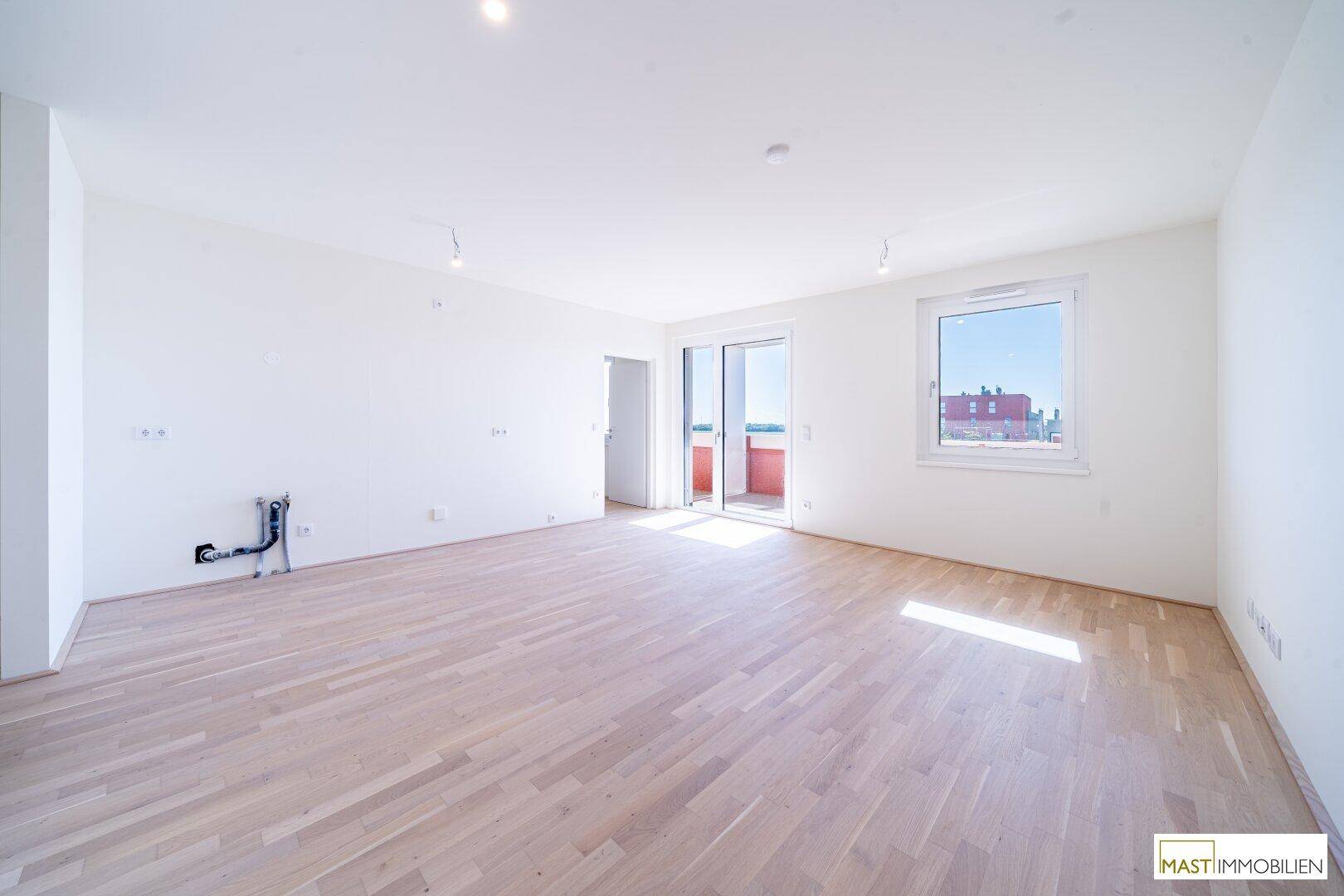 Geräumiges, helles Wohnzimmer mit hellem Parkettboden und direktem Zugang zum Balkon.