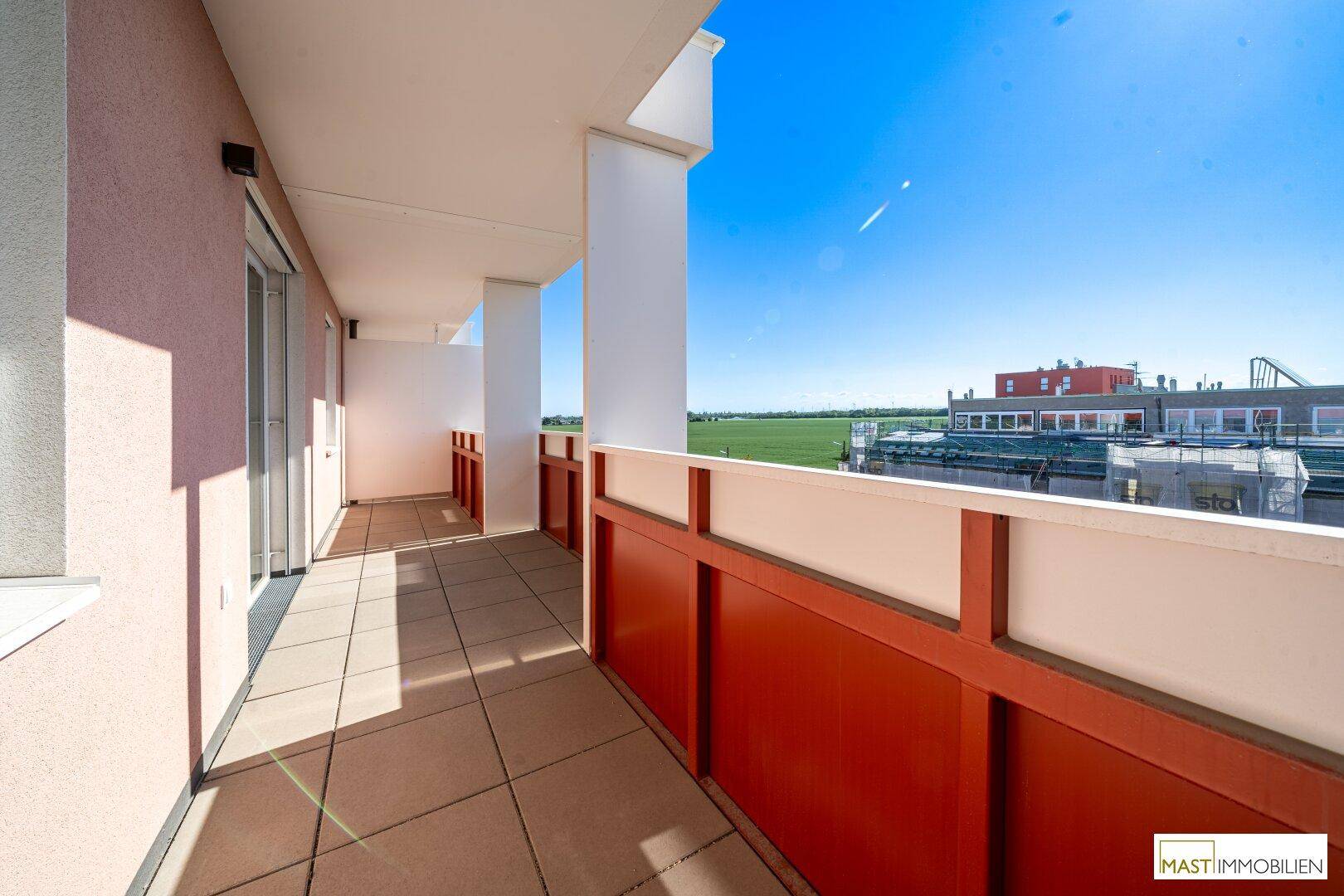 Langer Balkon mit Fliesenboden und rotem Geländer, bietet einen weiten Blick ins Grüne.