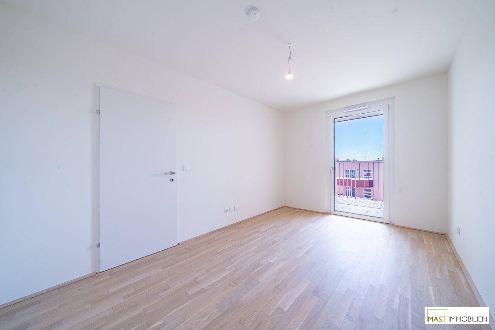 Geräumiges Zimmer mit hellem Parkettboden und Zugang zu einem Außenbereich, ideal als Schlafzimmer.