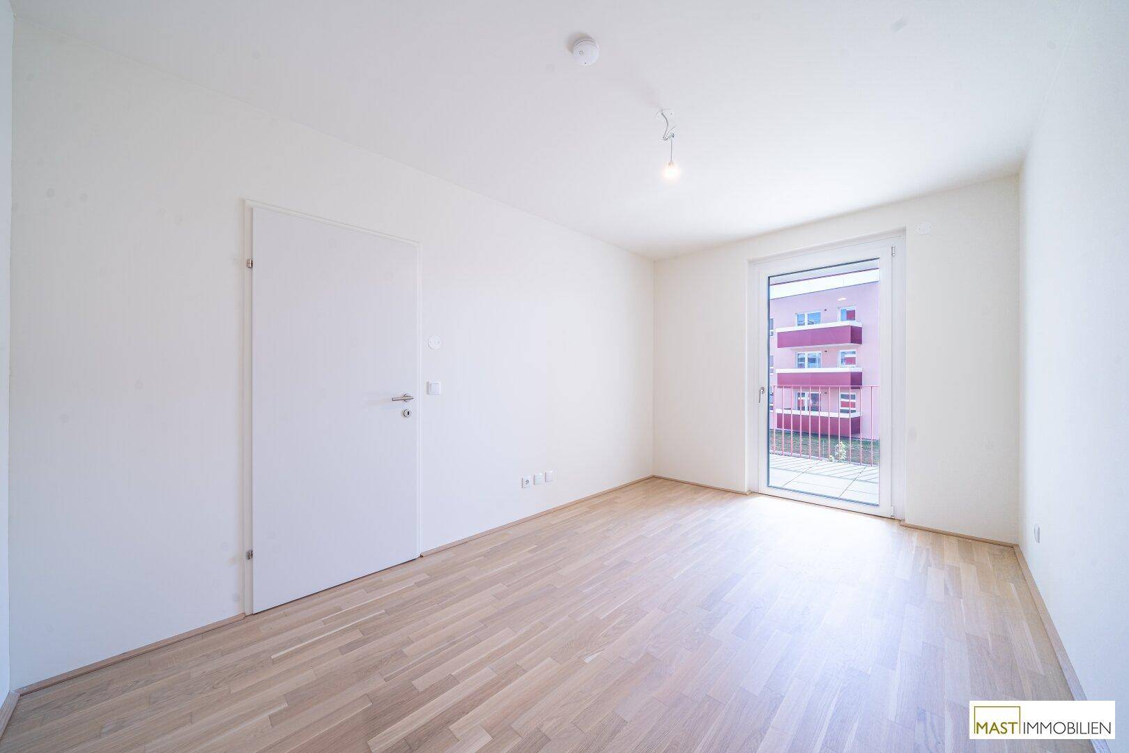 Helles Schlafzimmer mit Parkettboden und direktem Zugang zu einem Balkon, ideal für Morgenlicht.