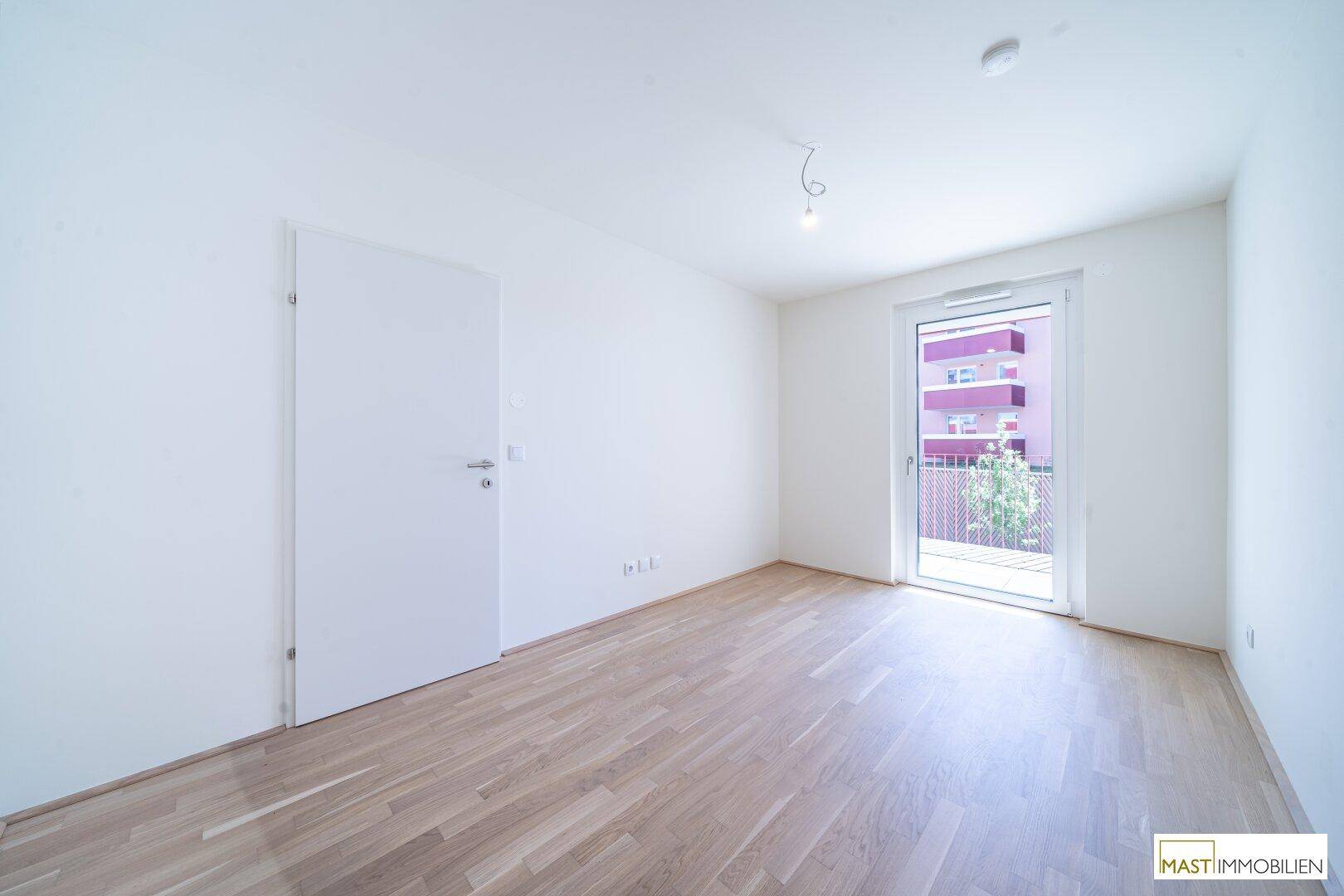 Helles Schlafzimmer mit Parkettboden, weißen Wänden und direktem Zugang zu einem Außenbereich.