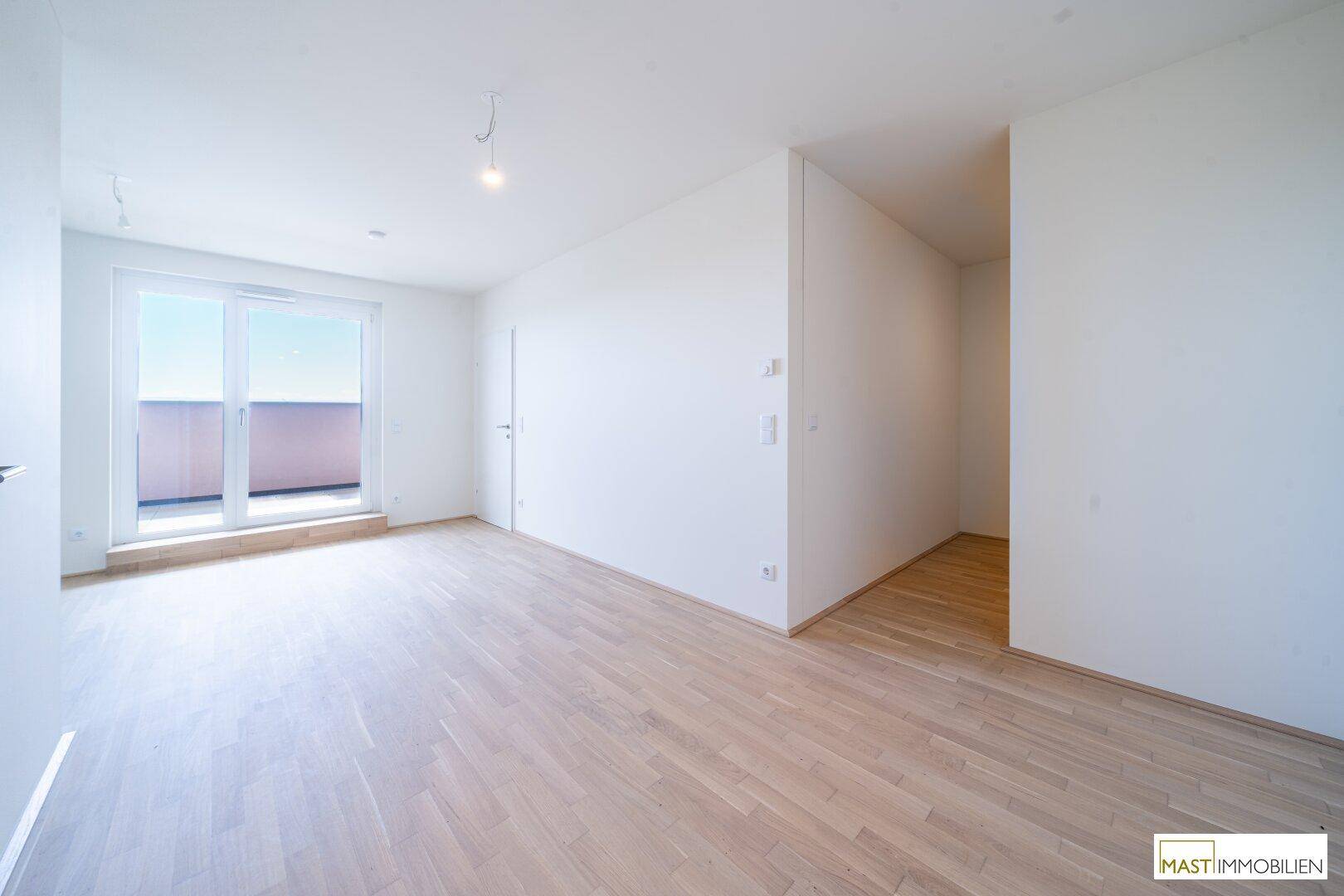 Heller, leerer Wohnraum mit Eichenparkett und Zugang zu einem Balkon oder einer Terrasse.