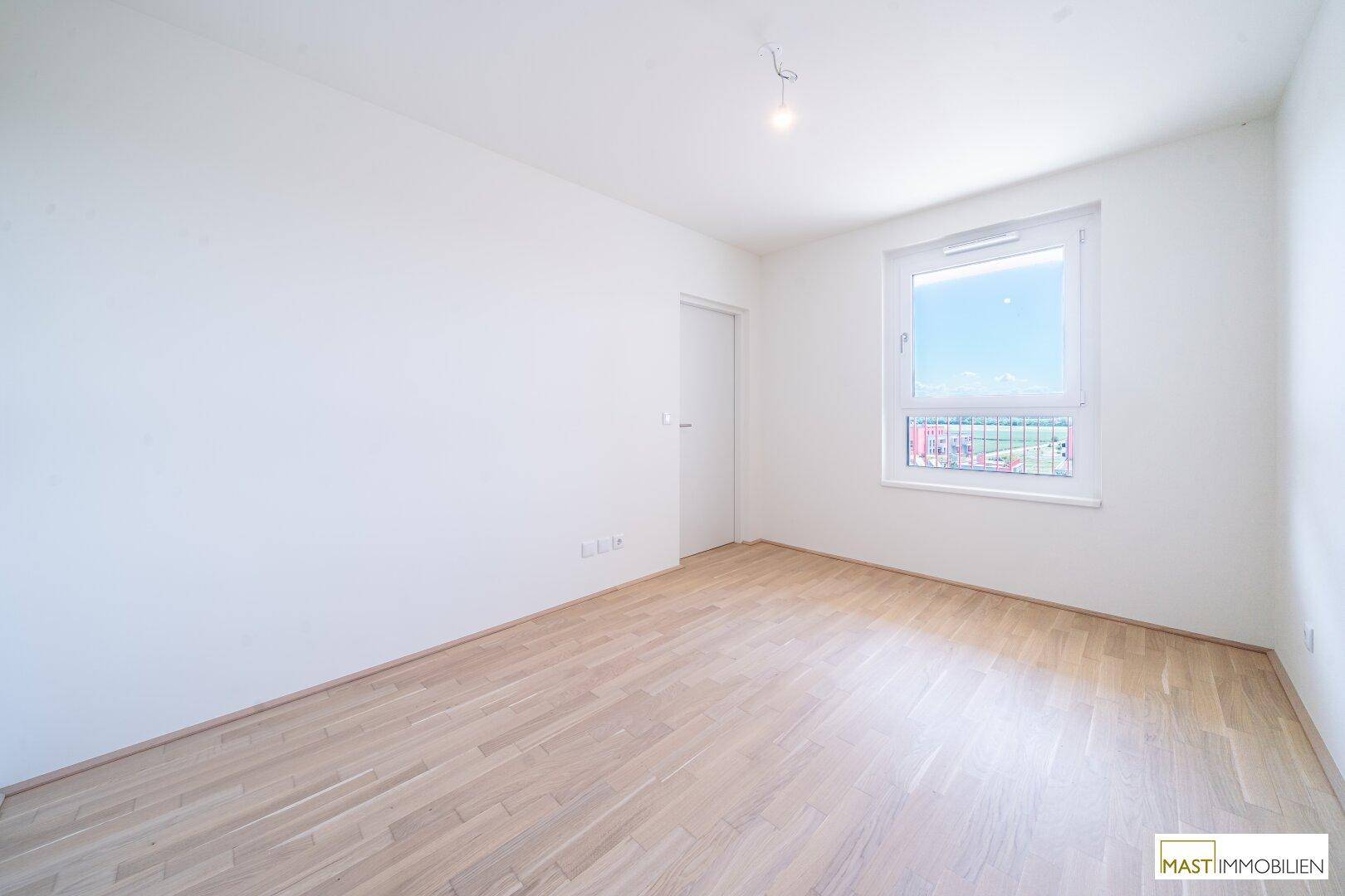 Helles Schlafzimmer mit Eichenparkett und einem Fenster, das viel Tageslicht hereinlässt.
