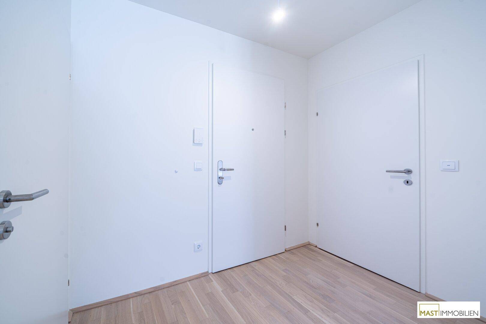 Heller Flur mit weiß gestrichenen Wänden und hellem Holzparkettboden.
