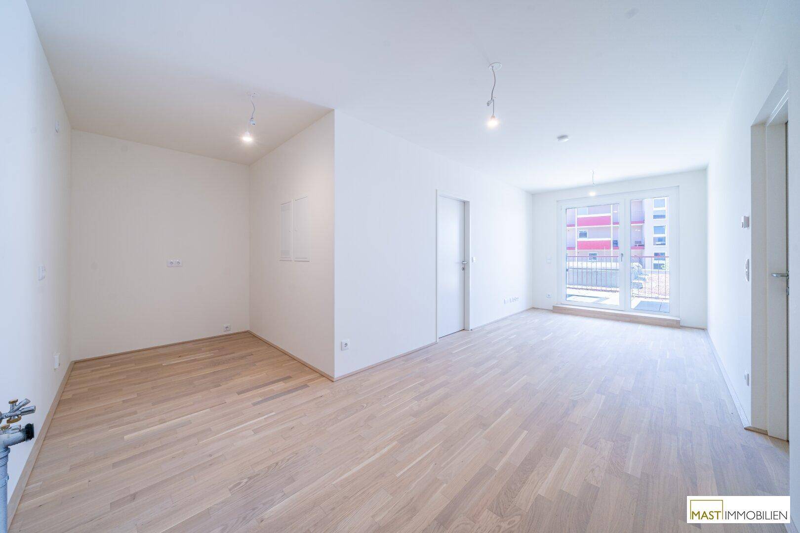 Heller, leerer Raum mit hellem Parkettboden und Zugang zu einem Balkon oder einer Terrasse.