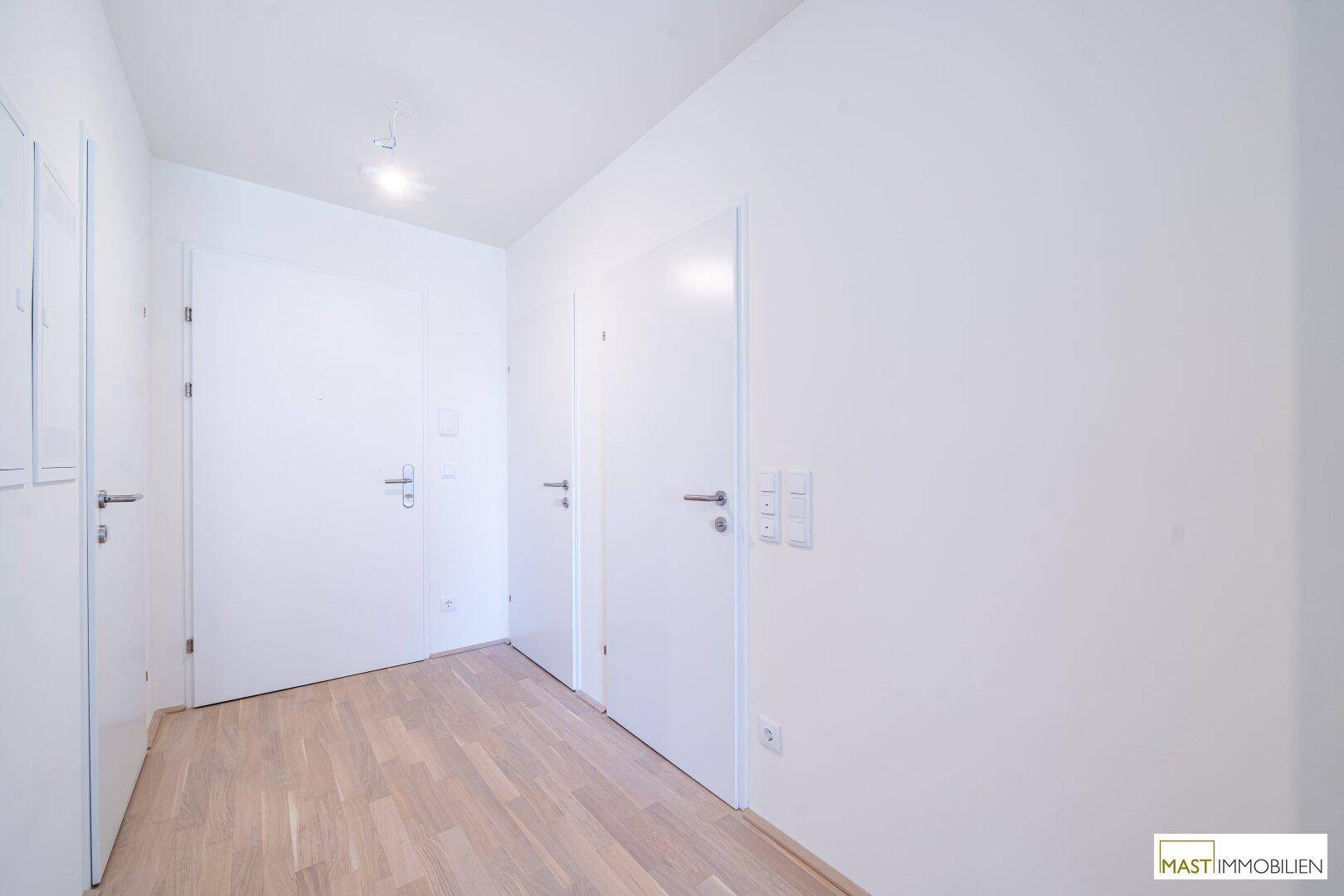 Heller Eingangsbereich mit modernem Holzboden und mehreren weißen Türen.