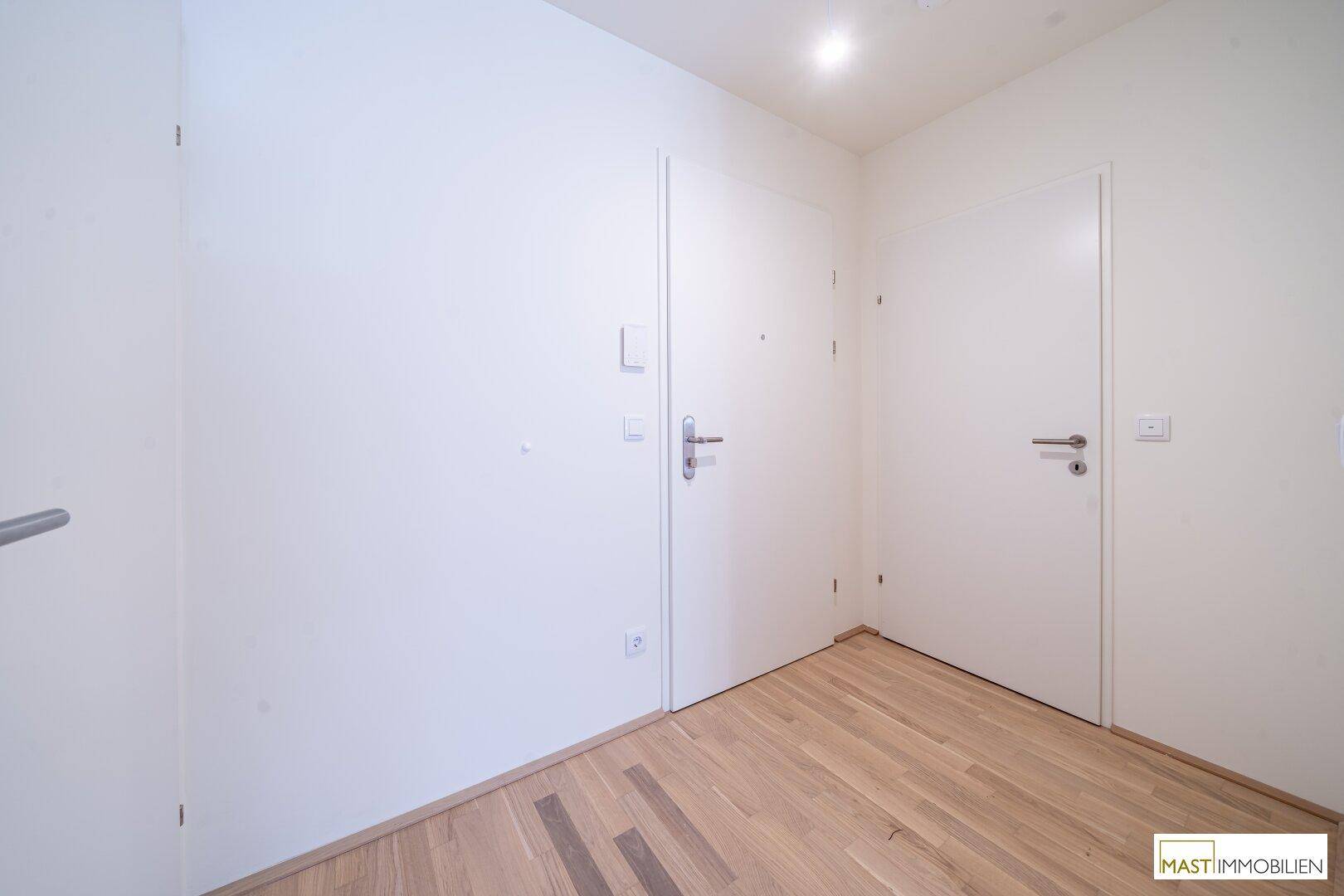 Heller Flur mit weiß gestrichenen Wänden und elegantem Holzparkettboden.