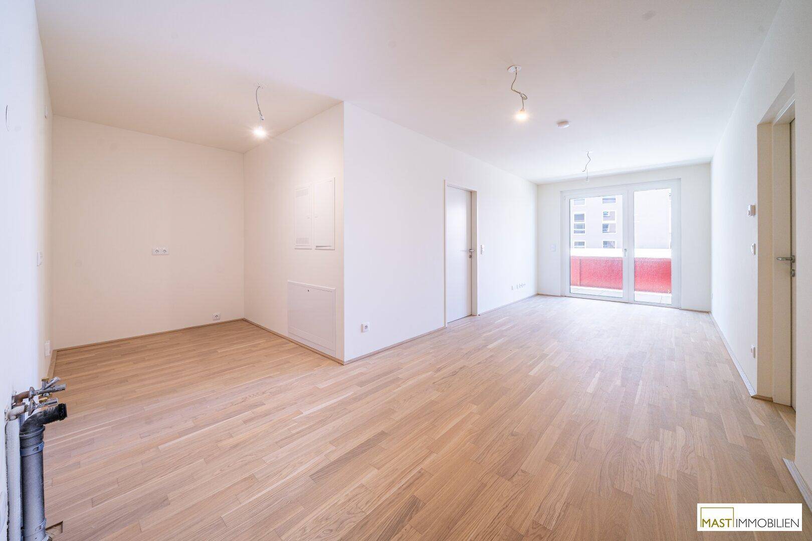 Heller Raum mit Parkettboden und Anschlüssen für eine Küche, mit Zugang zum Balkon.