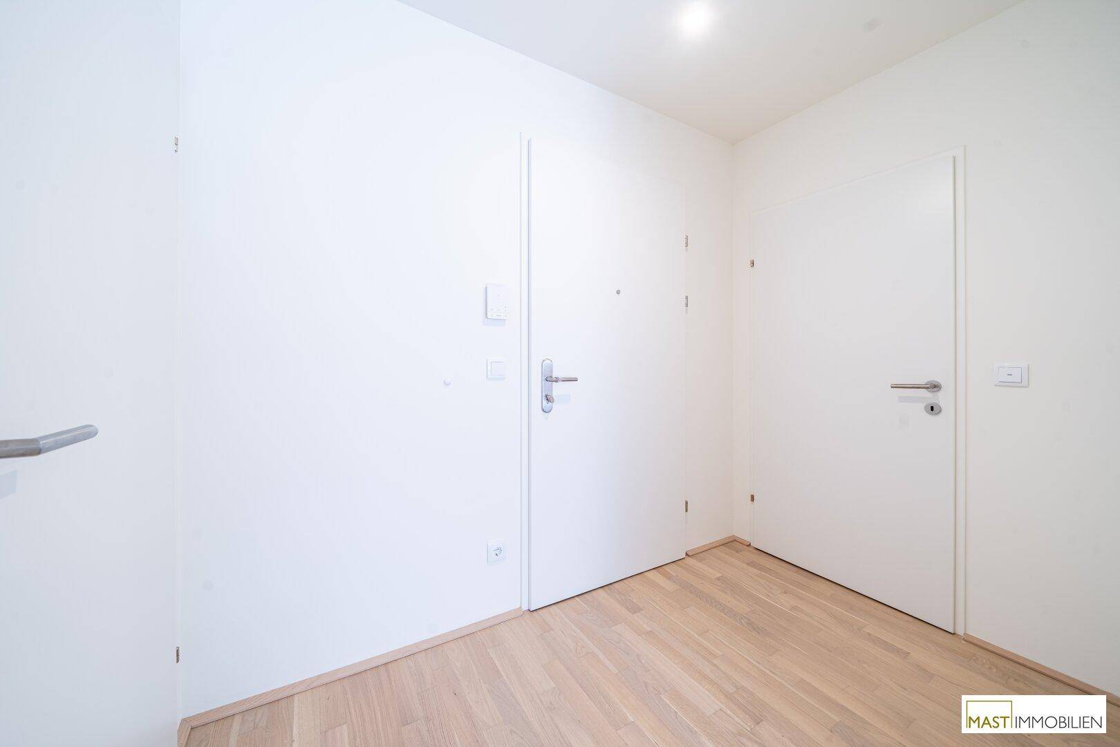 Heller Flur mit zwei weißen Türen und modernem hellen Holzparkettboden.