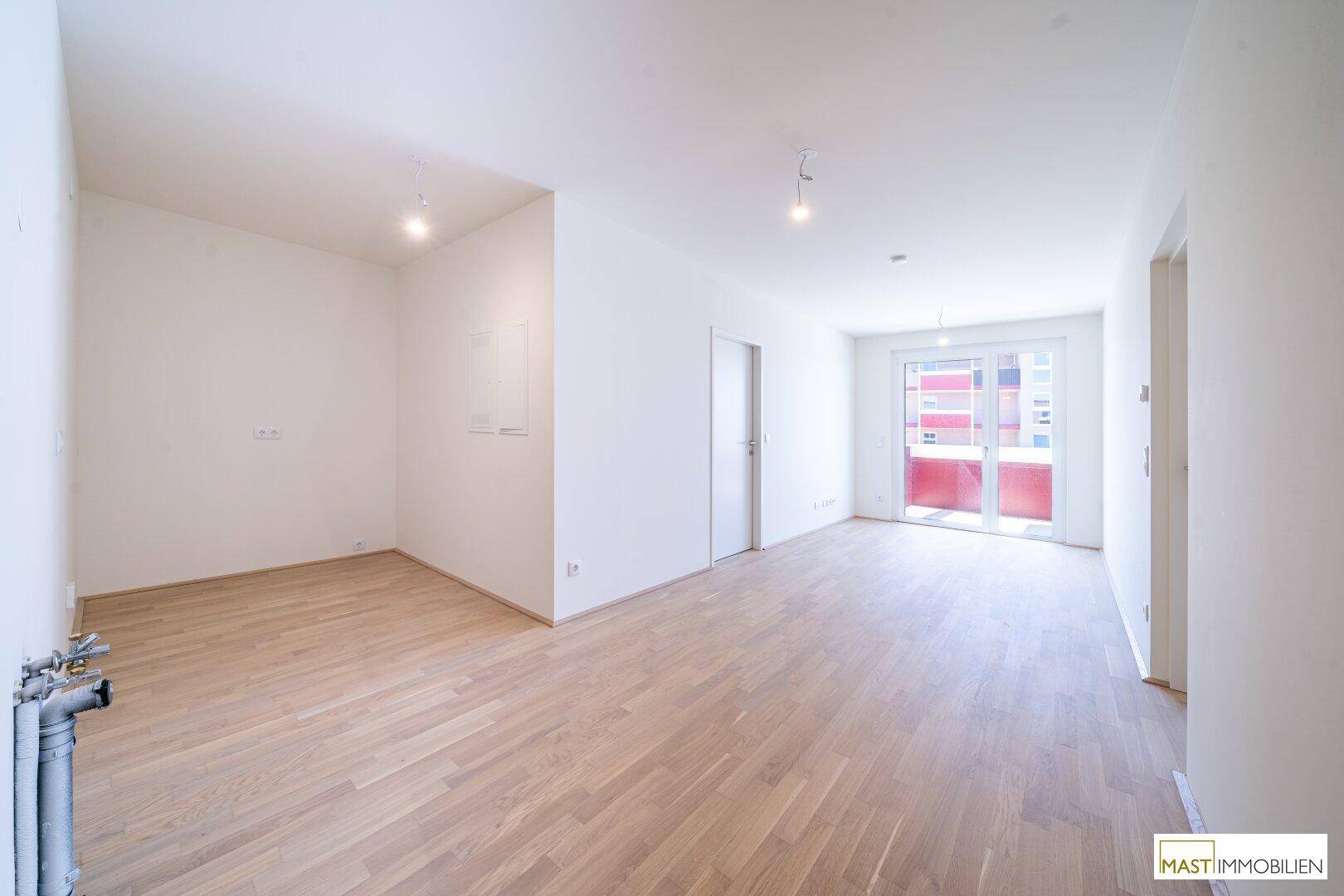 Geräumiger, heller Raum mit Holzparkettboden und Zugang zu einem Balkon oder einer Terrasse.