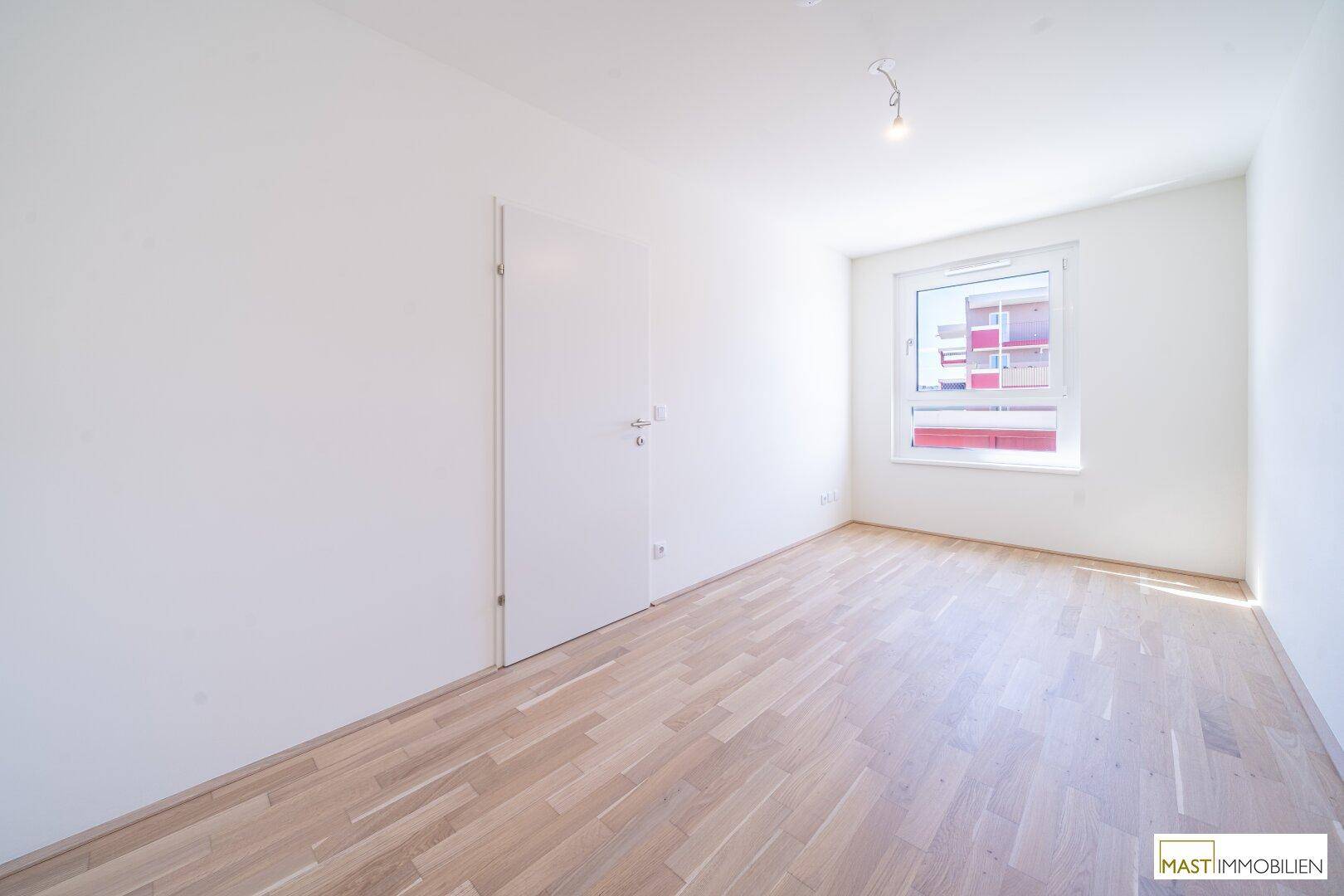 Unmöbliertes Zimmer mit hellem Holzfußboden und weiß gestrichenen Wänden, bereit zum Einzug.