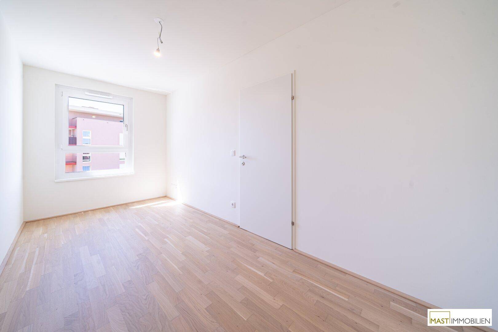 Helles, leeres Schlafzimmer mit Holzboden und weiß gestrichenen Wänden.