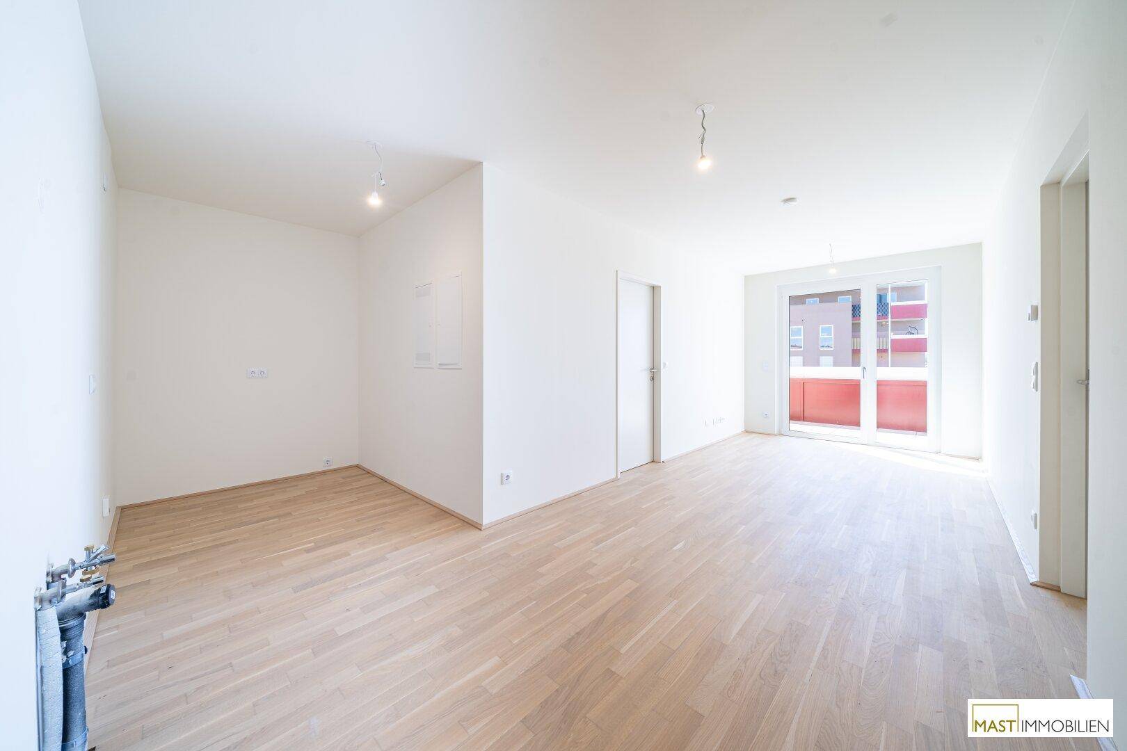 Heller, leerer Wohnbereich mit hellem Parkettboden und Zugang zu einem Balkon.