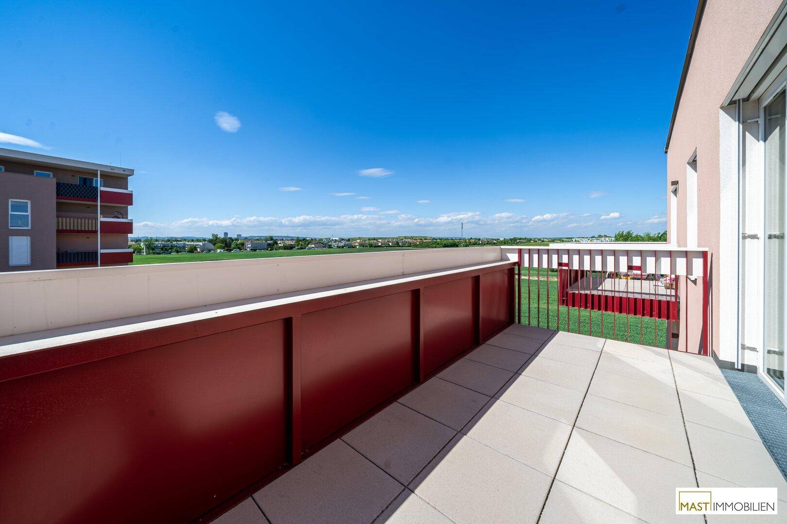 Sonnige Terrasse mit Fliesenboden und weitem Blick über die grüne Landschaft.