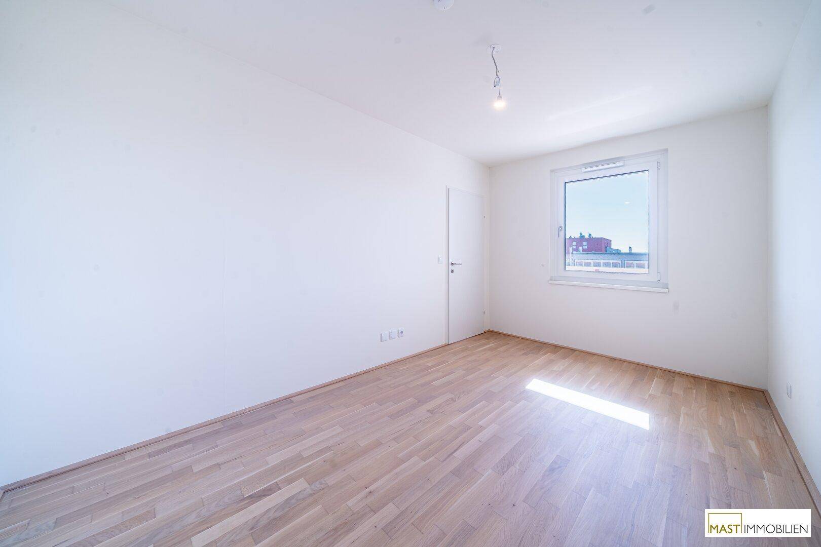 Leeres Schlafzimmer mit hellem Parkettboden, weiß gestrichenen Wänden und Fenster.