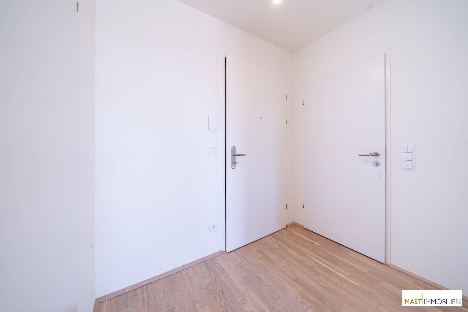 Heller Eingangsbereich mit zwei weißen Türen und modernem Holzparkettboden.