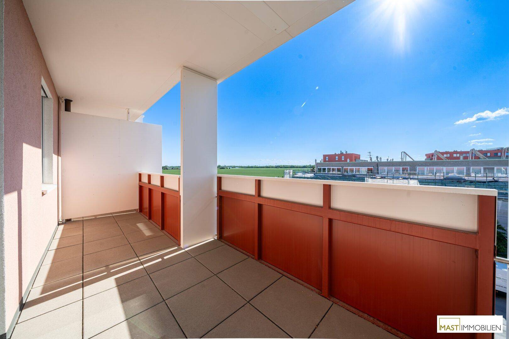Sonniger Balkon mit Fliesenboden und weitem Ausblick auf die umliegende Landschaft.