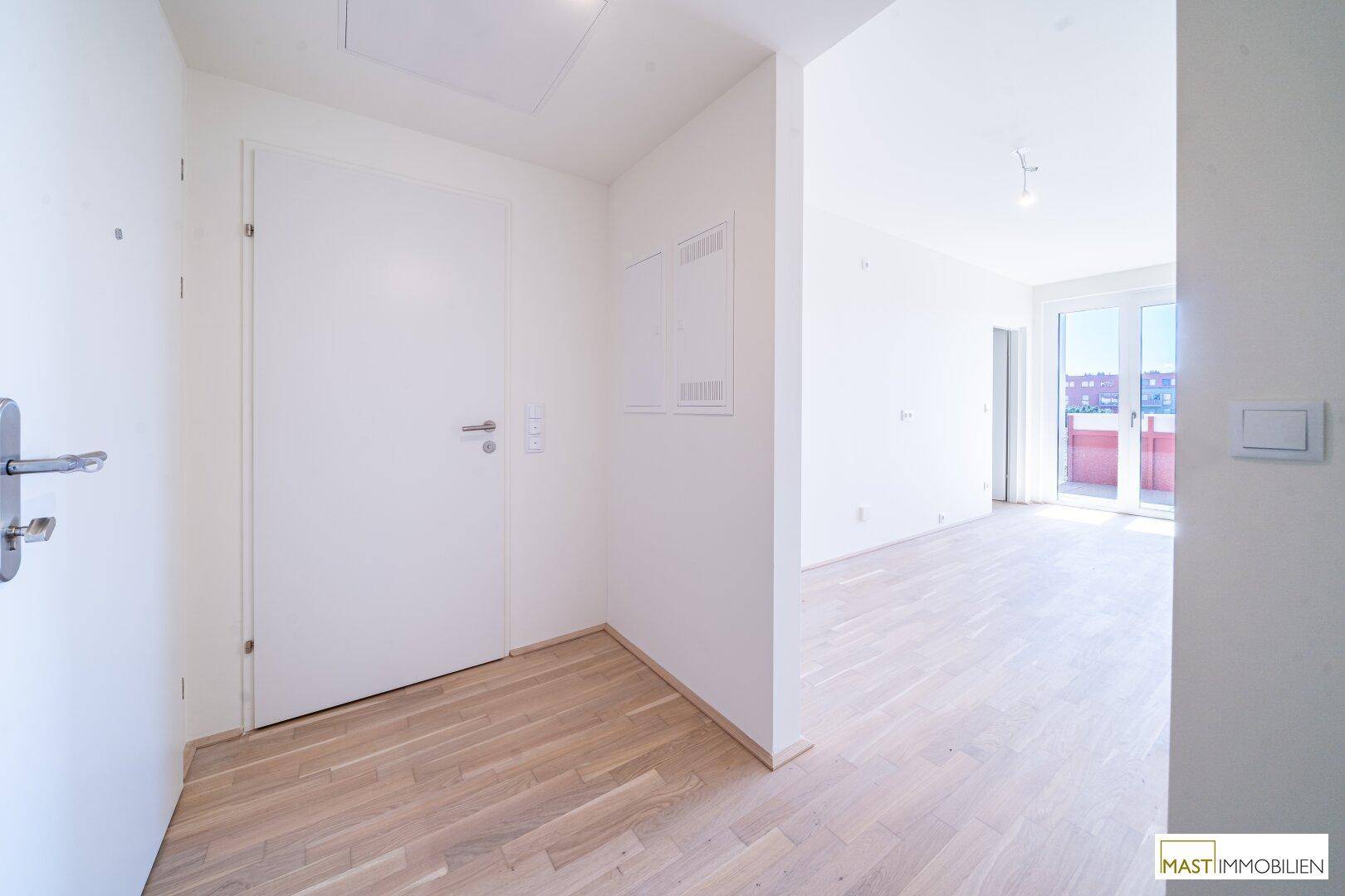 Heller Eingangsbereich mit Holzboden und Zugang zu den Wohnräumen und einem Balkon.