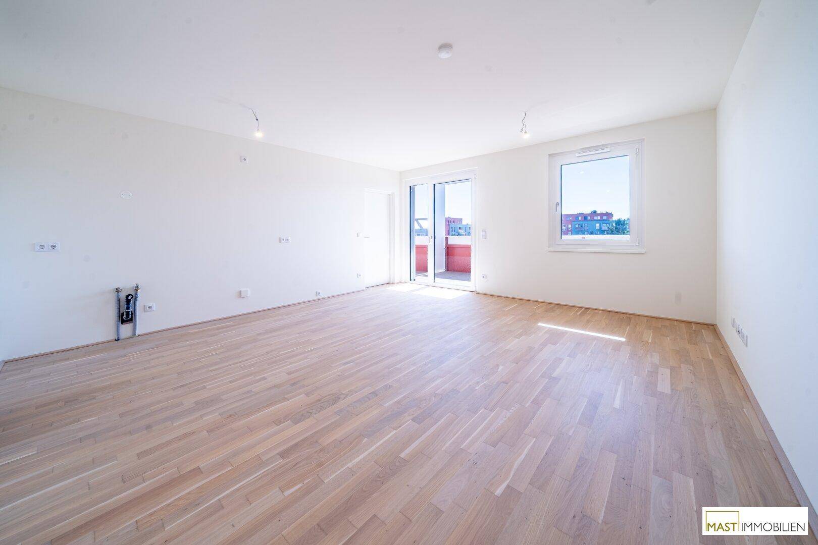 Geräumiges, helles Wohnzimmer mit Holzboden, großen Fenstern und Zugang zum Balkon.