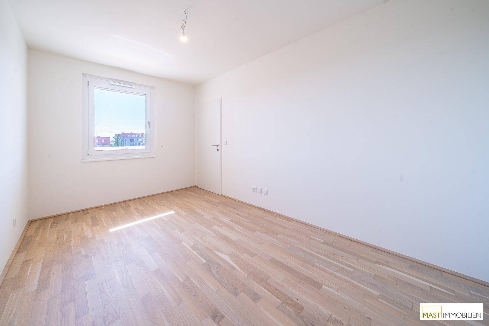 Helles Schlafzimmer mit Holzboden und einem großen Fenster, das viel Tageslicht hereinlässt.