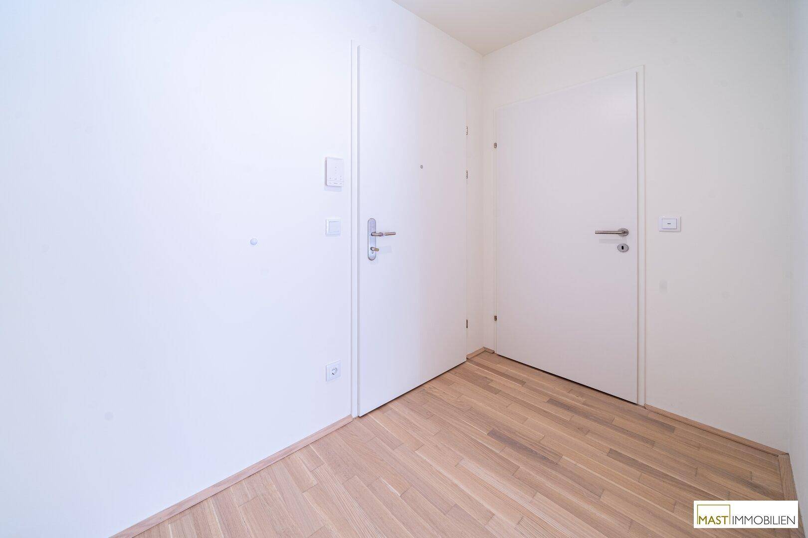 Heller Flur mit zwei weißen Türen und modernem Parkettboden in einem Neubau.