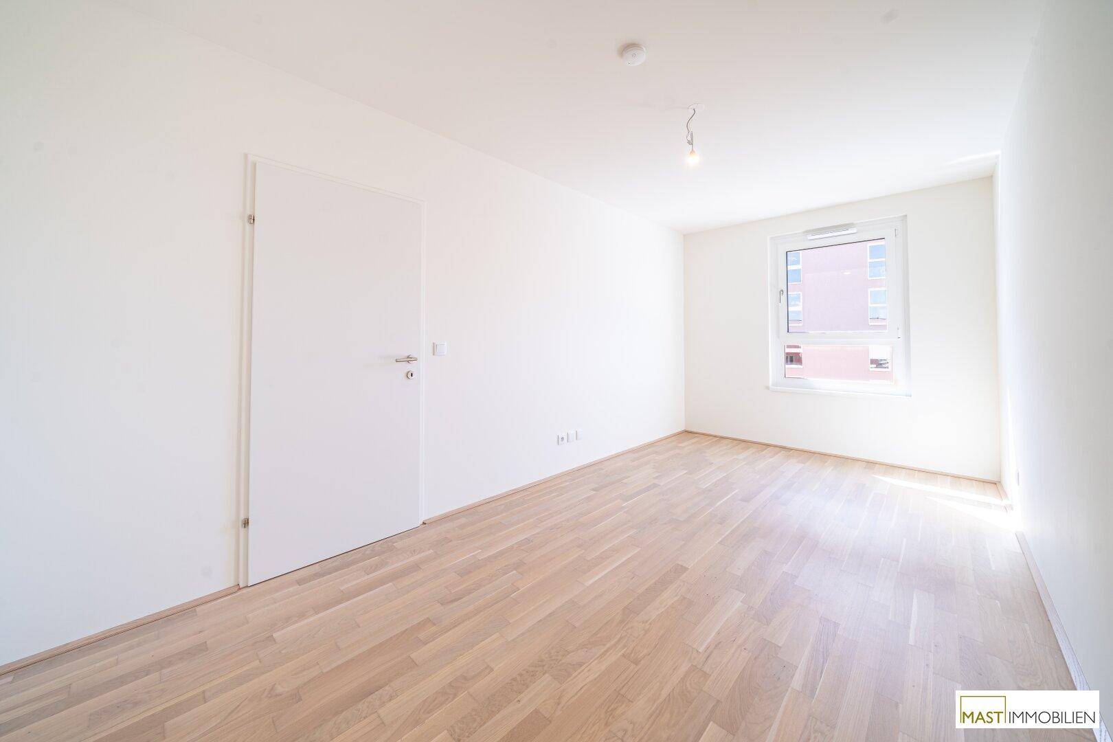 Helles Schlafzimmer mit Parkettboden und einem Fenster, das viel Tageslicht hereinlässt.