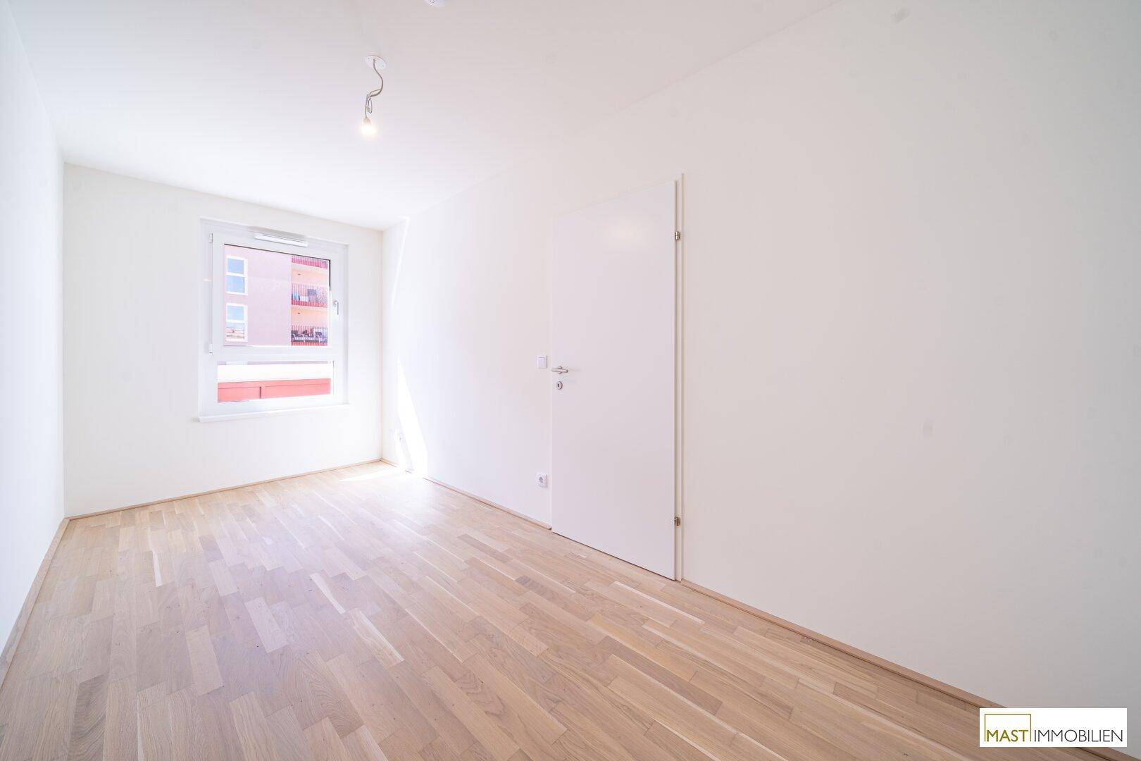 Weiteres helles Zimmer mit Parkettboden und einem großen Fenster, ideal als Schlaf- oder Arbeitszimmer.