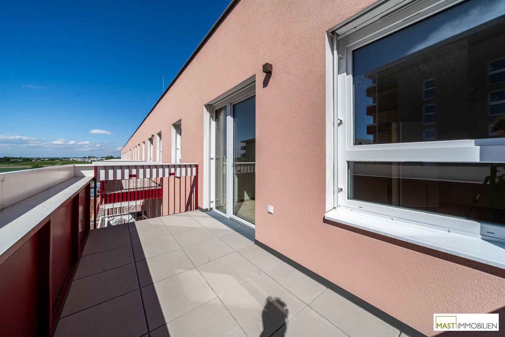 Langer Balkon mit Fliesenboden und Blick auf die moderne Fassade des Gebäudes und die Umgebung.