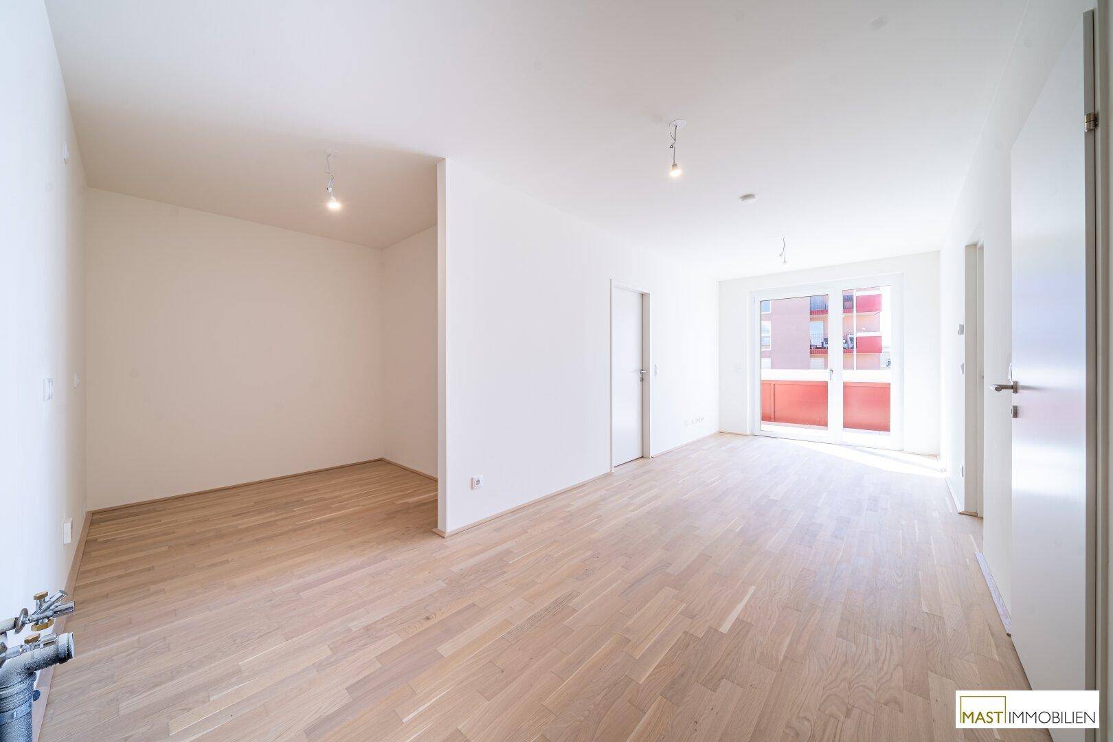 Großzügiger, heller Wohnbereich mit Eichenparkett und Zugang zu einem Balkon, ideal für offenes Wohnen.