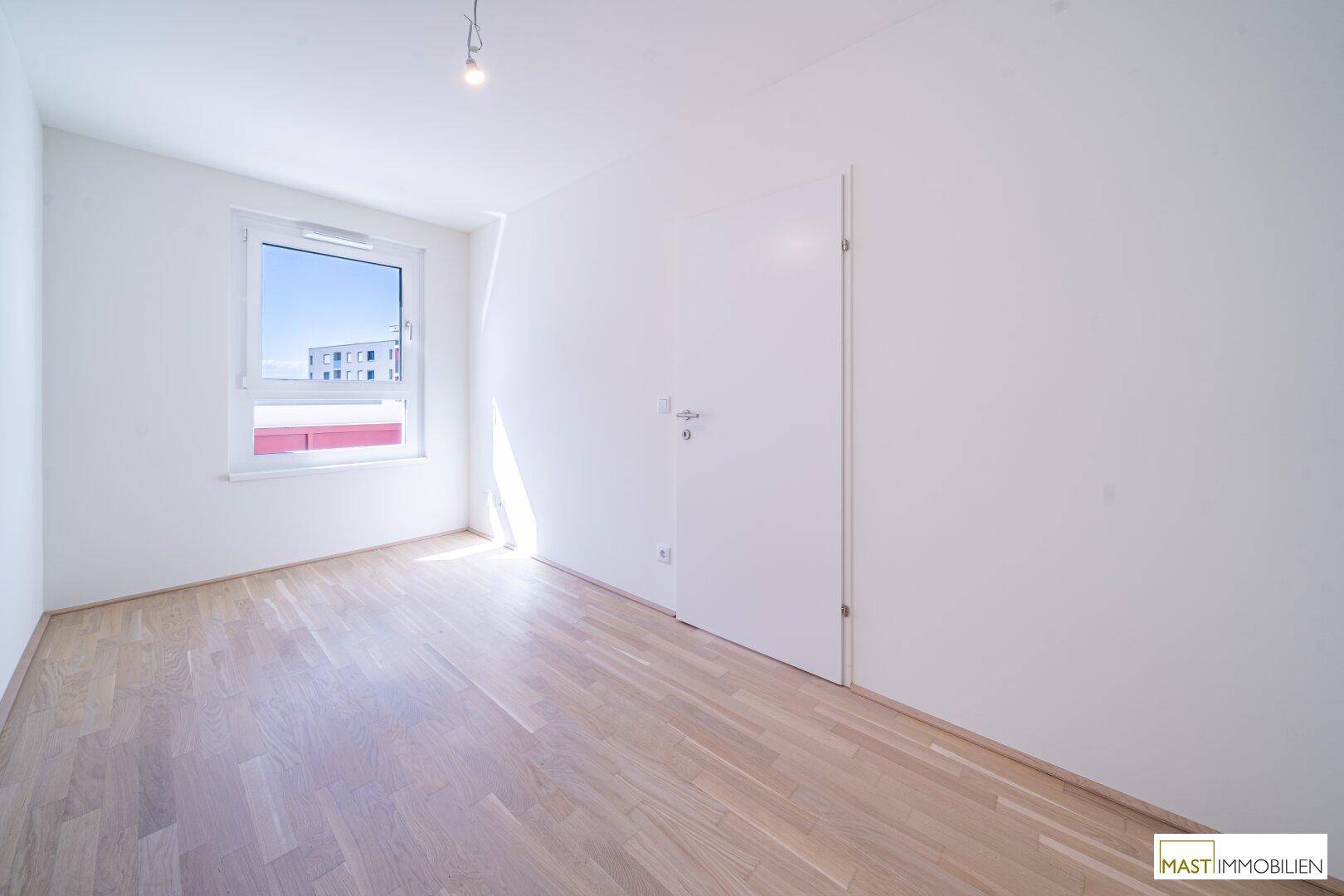 Helles Schlafzimmer mit neuem Holzparkettboden und einem großen Fenster, das viel Tageslicht hereinlässt.