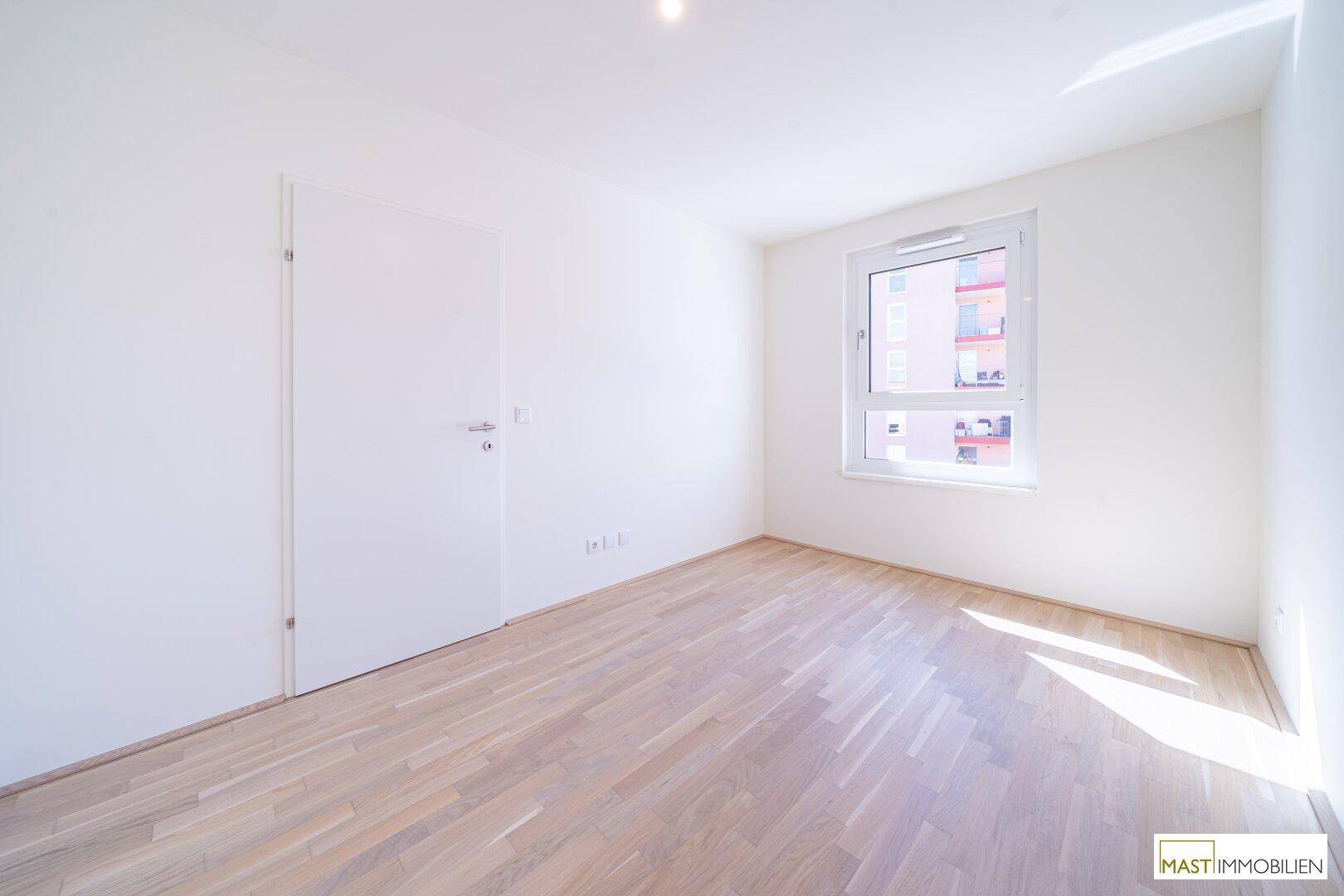 Freundliches Zimmer mit hellem Holzparkett und einem Fenster, das eine angenehme Wohnatmosphäre schafft.