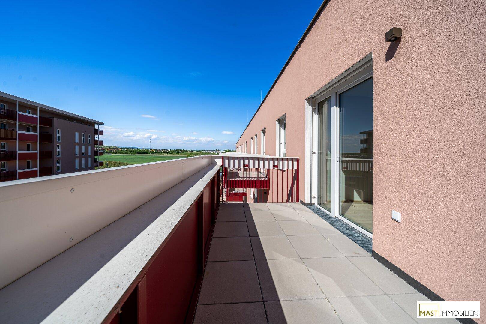 Langer Balkon mit Fliesenboden und weitem Blick über die Landschaft unter einem strahlend blauen Himmel.